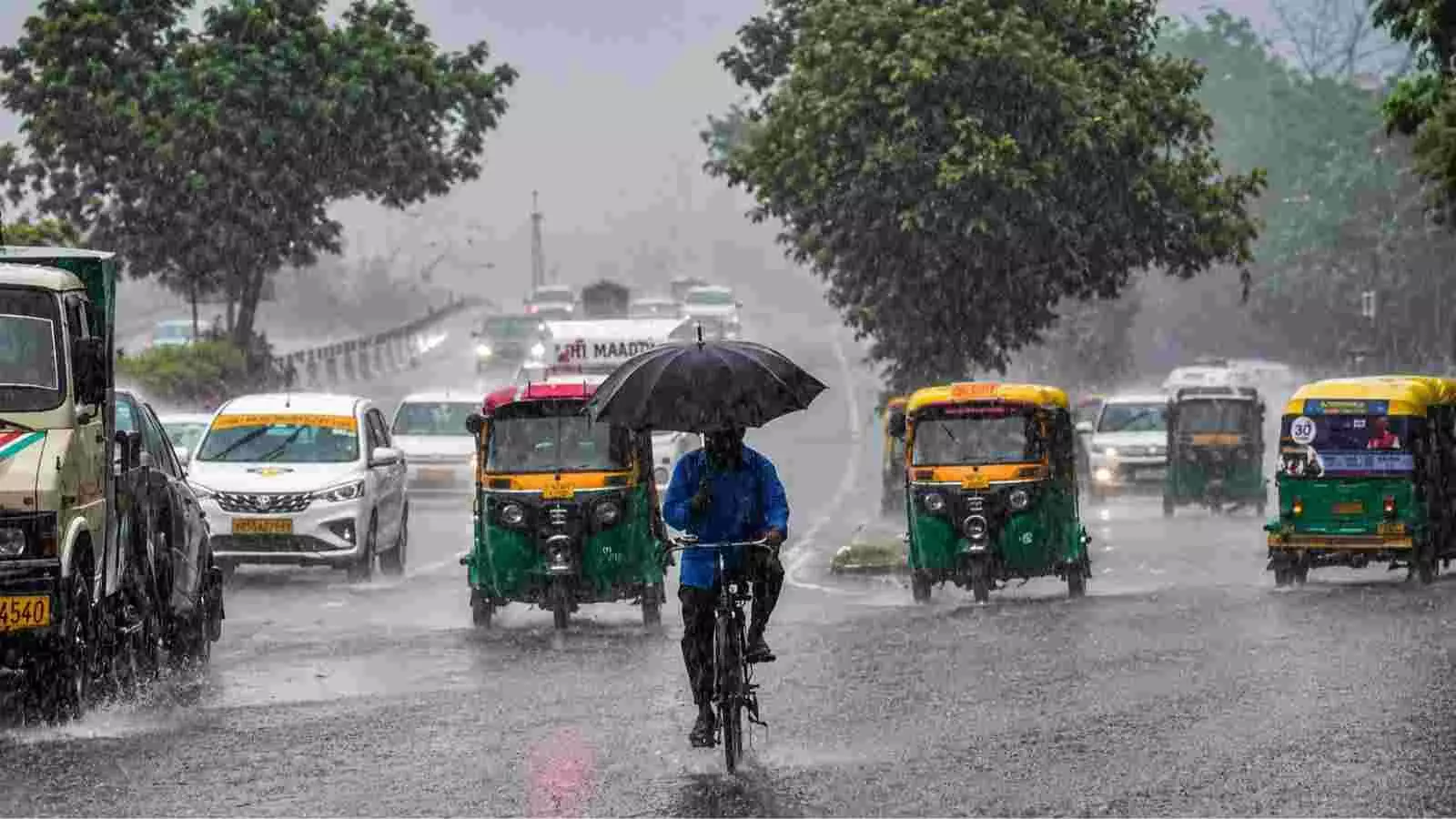 बारिश के दौरान सड़क पर साइकिल चलाते व्यक्ति का उत्तर भारत में दृश्य। बारिश के दौरान सड़क पर साइकिल चलाते व्यक्ति का उत्तर भारत में दृश्य।
