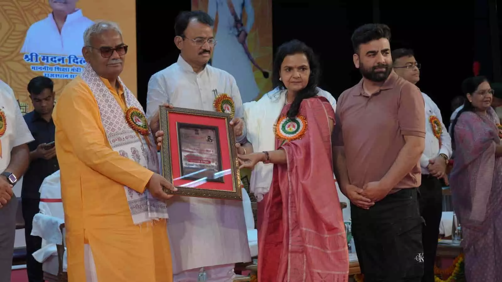 जयपुर में आयोजित समारोह में मंच पर फ्रेम किया हुआ पुरस्कार ग्रहण करतीं महिला।