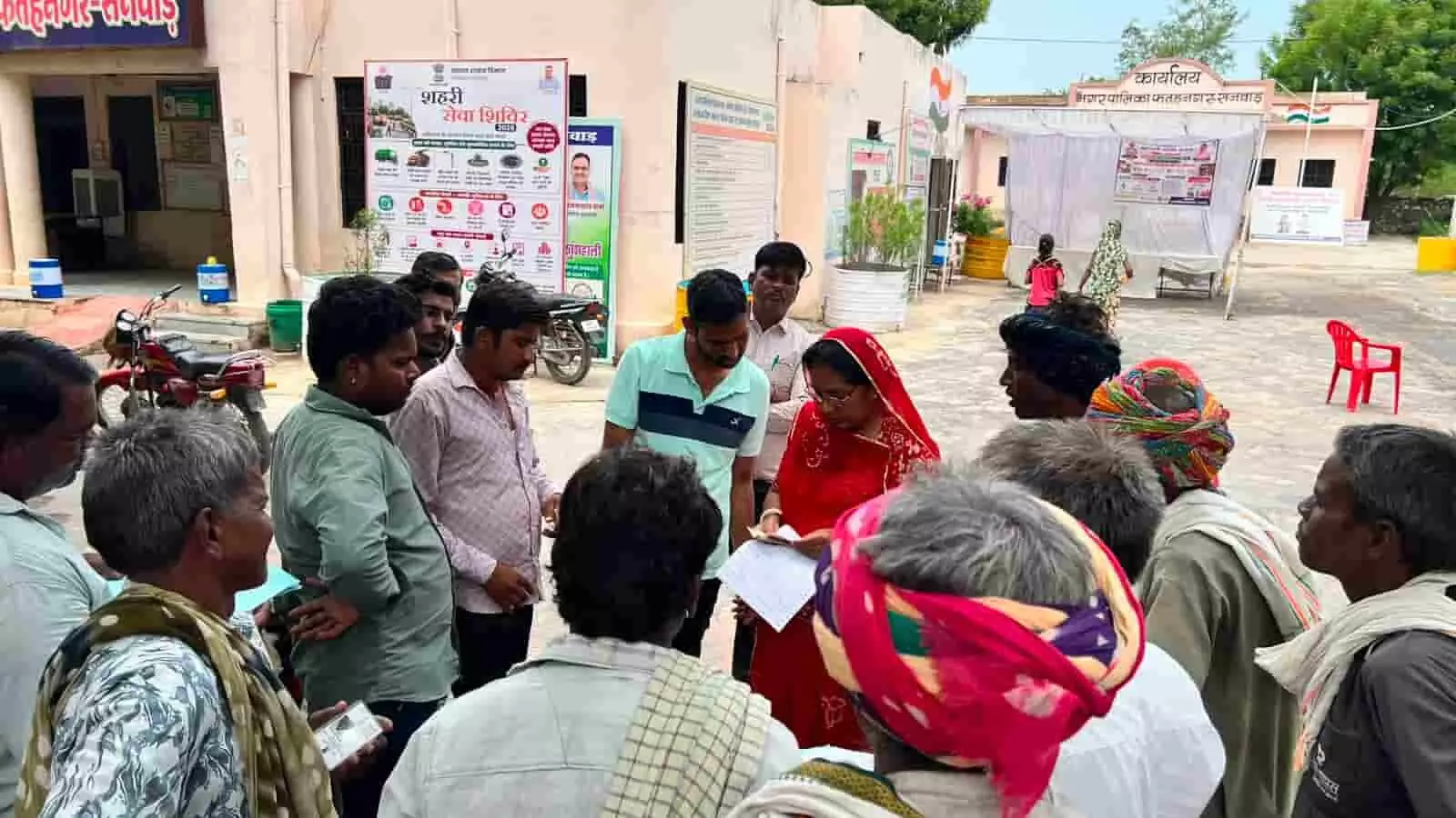 नगरपालिका परिसर में लोगों की भीड़ के बीच दस्तावेजों को देखती महिला अधिकारी।