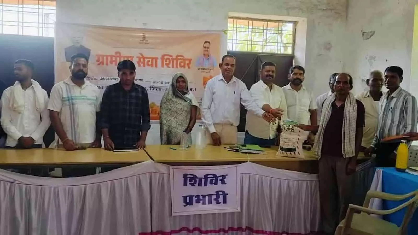 ग्रामीण सेवा शिविर में मंच पर उपस्थित अधिकारी एक ग्रामीण को योजना का लाभ प्रदान करते हुए।