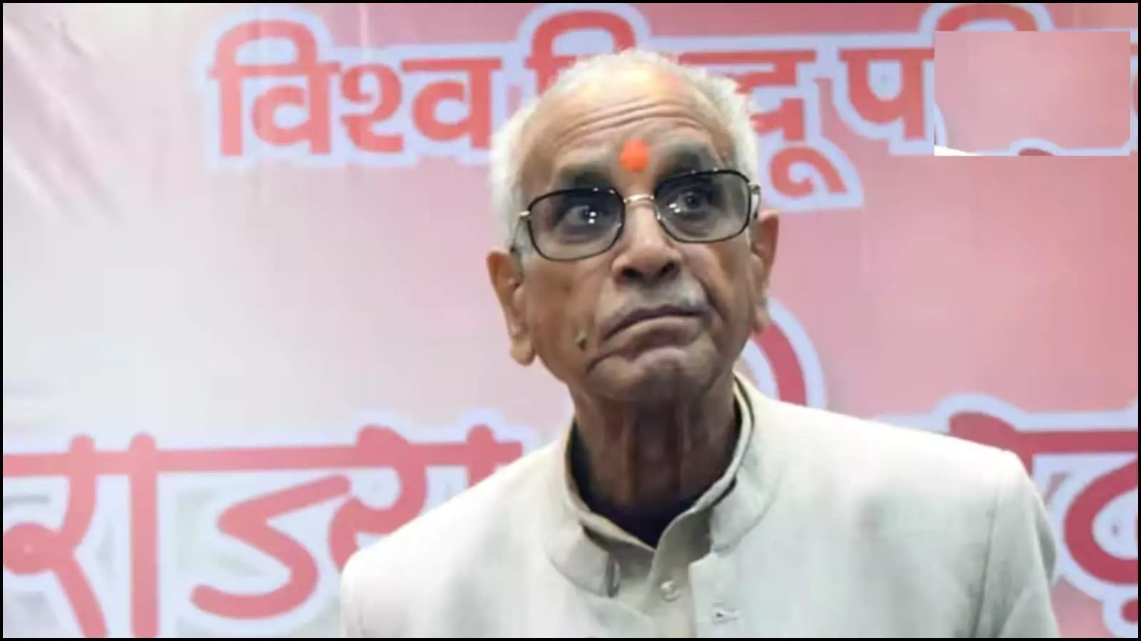 अक्षरयुक्त लाल पृष्ठभूमि के सामने चश्मा और तिलक लगाए चंपत राय अयोध्या में उपस्थित।