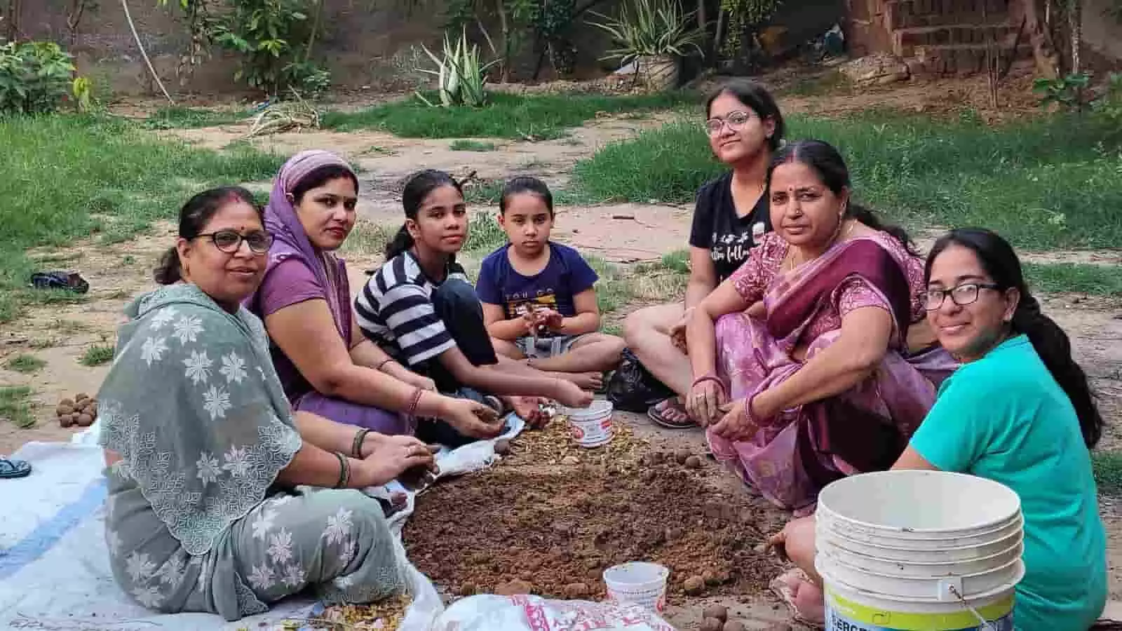 जमीन पर बैठकर मिट्टी से सीड बॉल बनातीं महिलाएं और बच्चे पर्यावरण संरक्षण अभियान के अंतर्गत। जमीन पर बैठकर मिट्टी से सीड बॉल बनातीं महिलाएं और बच्चे पर्यावरण संरक्षण अभियान के अंतर्गत।