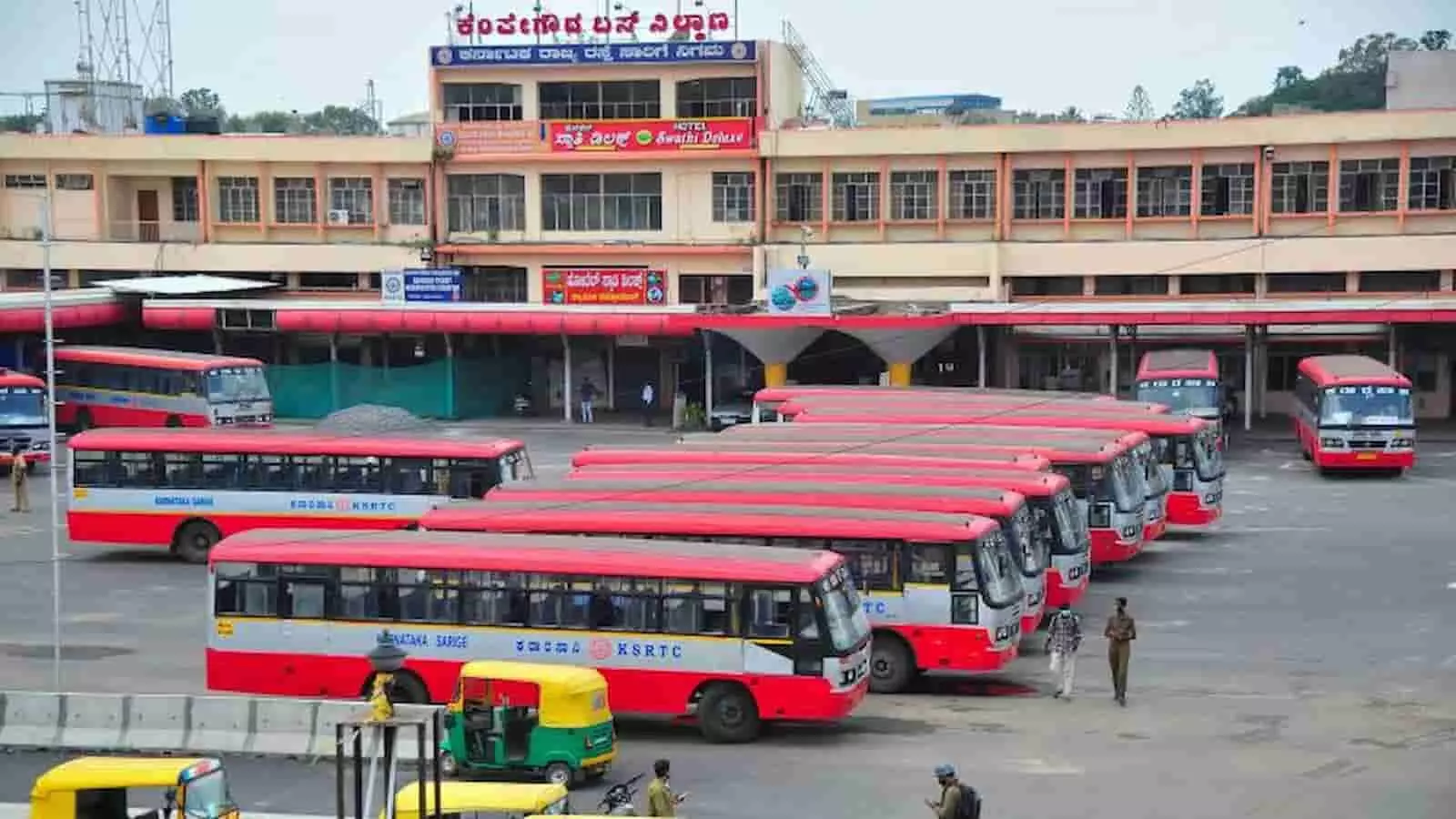बस टर्मिनल पर खड़ी लाल रंग की केएसआरटीसी बसों और लोगों की तस्वीर।