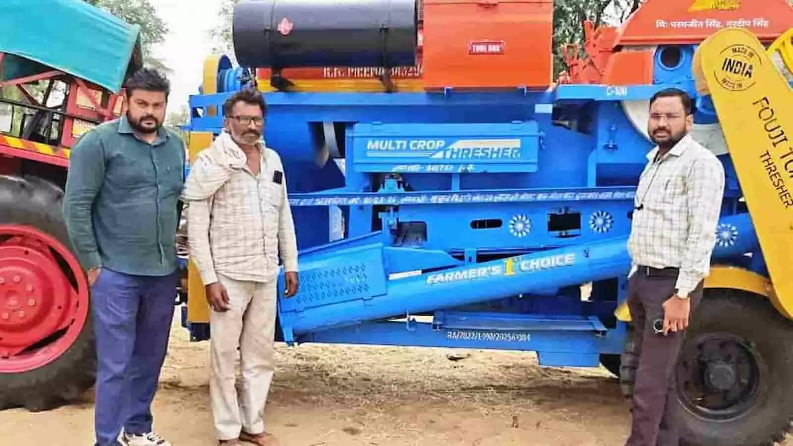 तस्वीर में एक नीले रंग के मल्टी क्रॉप थ्रेसर कृषि यंत्र के पास खड़े तीन पुरुष। तस्वीर में एक नीले रंग के मल्टी क्रॉप थ्रेसर कृषि यंत्र के पास खड़े तीन पुरुष।