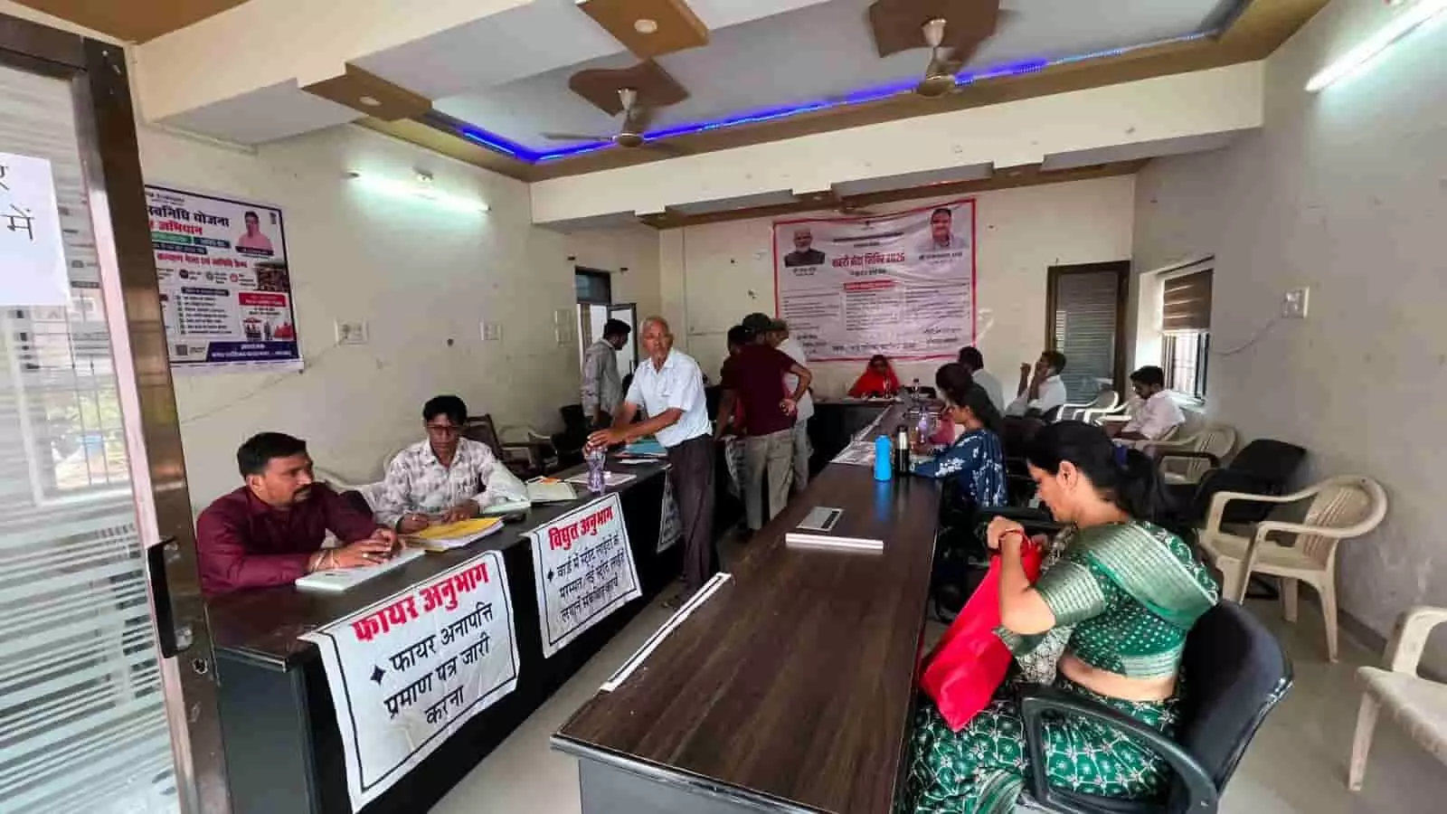 नगरपालिका परिसर के भीतर बने विभिन्न प्रशासनिक काउंटरों पर बैठकर कार्य करते अधिकारी और खड़े नागरिक।