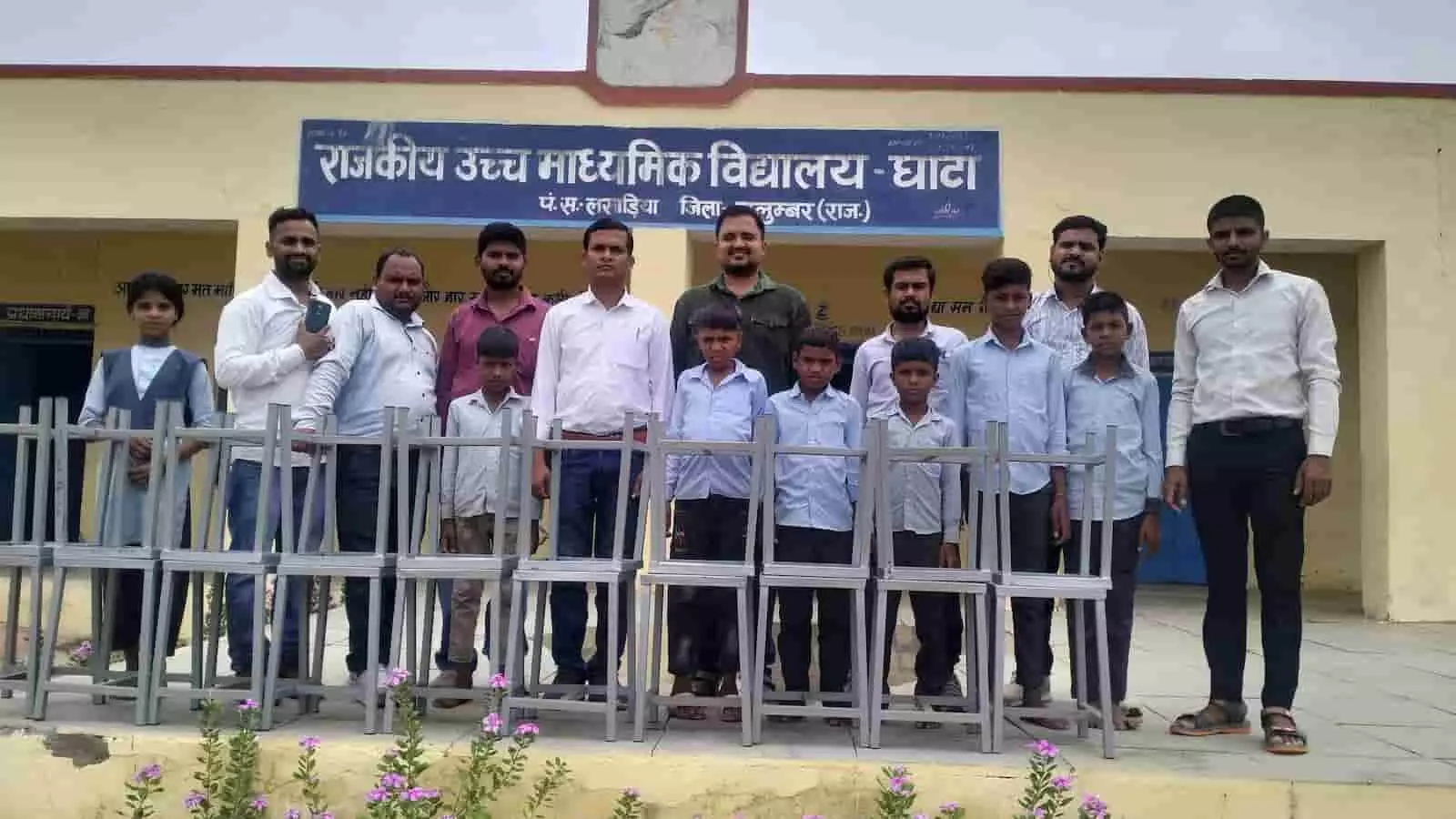 विद्यालय भवन के सामने भेंट किए गए स्टूलों के साथ खड़े शिक्षक और छात्र। विद्यालय भवन के सामने भेंट किए गए स्टूलों के साथ खड़े शिक्षक और छात्र।
