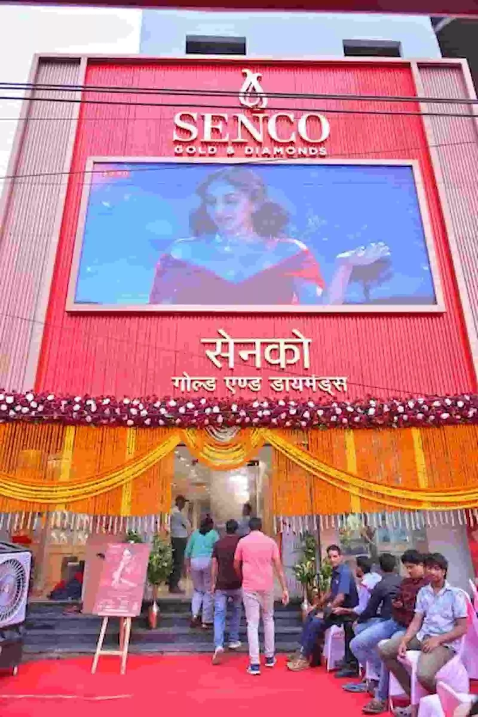 गेंदे के फूलों से सजा हुआ सेन्को गोल्ड एंड डायमंड्स का भव्य शोरूम प्रवेश द्वार और लोगों के साथ। गेंदे के फूलों से सजा हुआ सेन्को गोल्ड एंड डायमंड्स का भव्य शोरूम प्रवेश द्वार और लोगों के साथ।