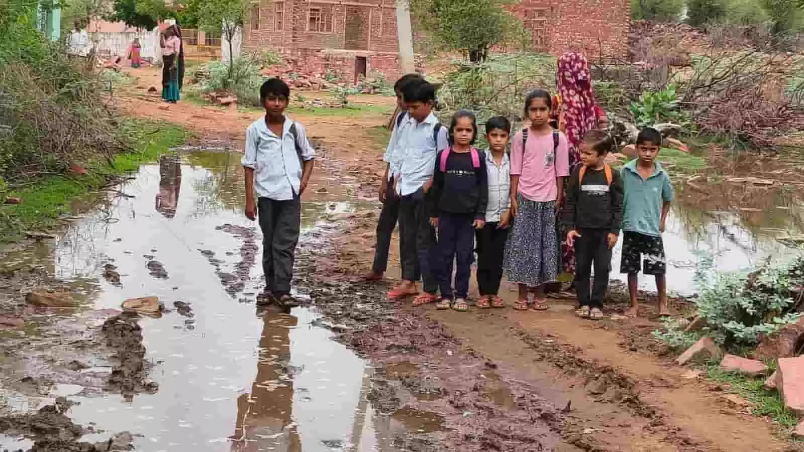 झिरका गांव में कीचड़ और जलभराव वाले रास्ते पर खड़े स्कूल जाते बच्चे। झिरका गांव में कीचड़ और जलभराव वाले रास्ते पर खड़े स्कूल जाते बच्चे।
