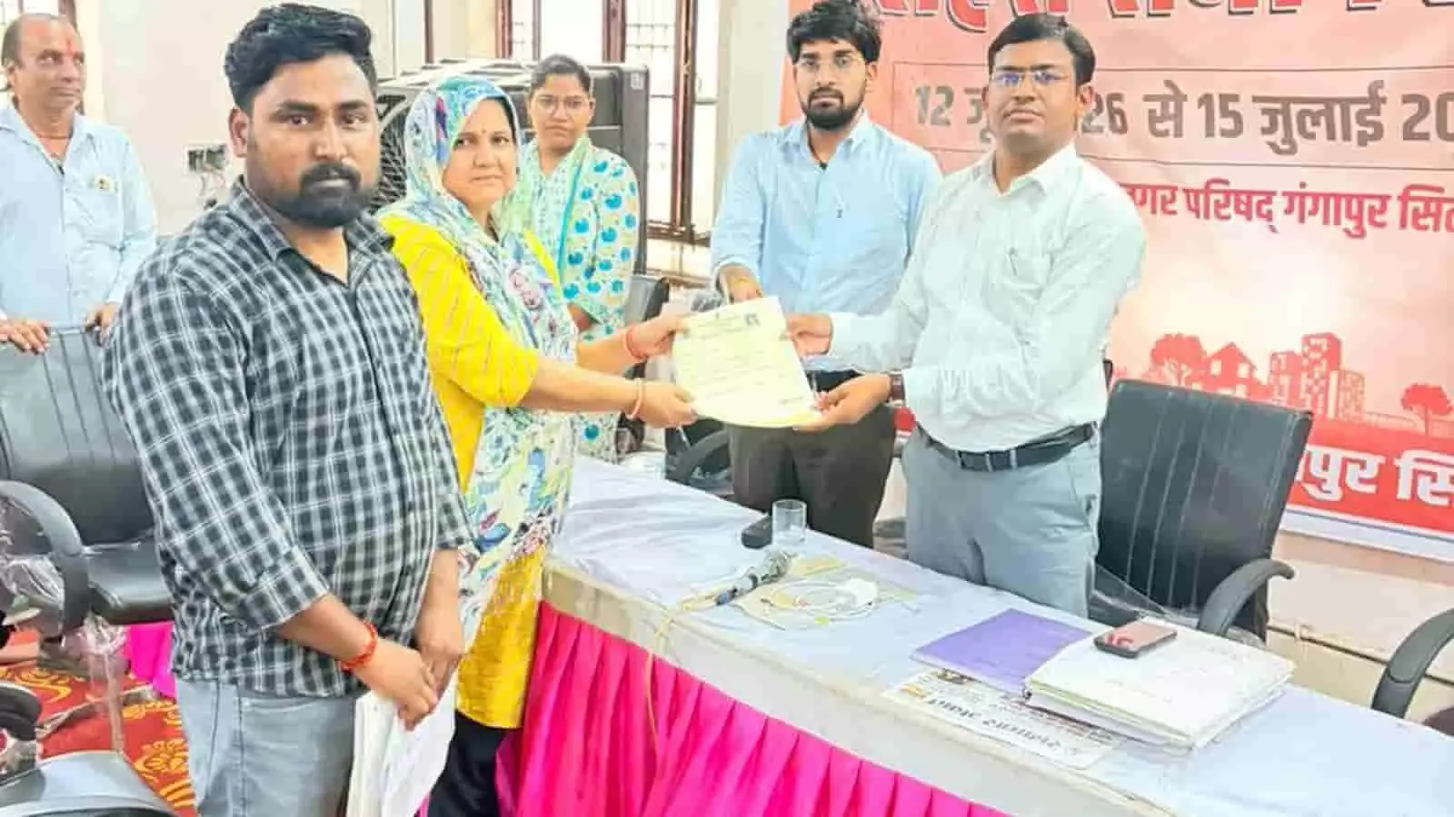 नगर परिषद के अधिकारी गंगापुर सिटी में शहरी सेवा शिविर के दौरान दस्तावेज सौंप रहे हैं।