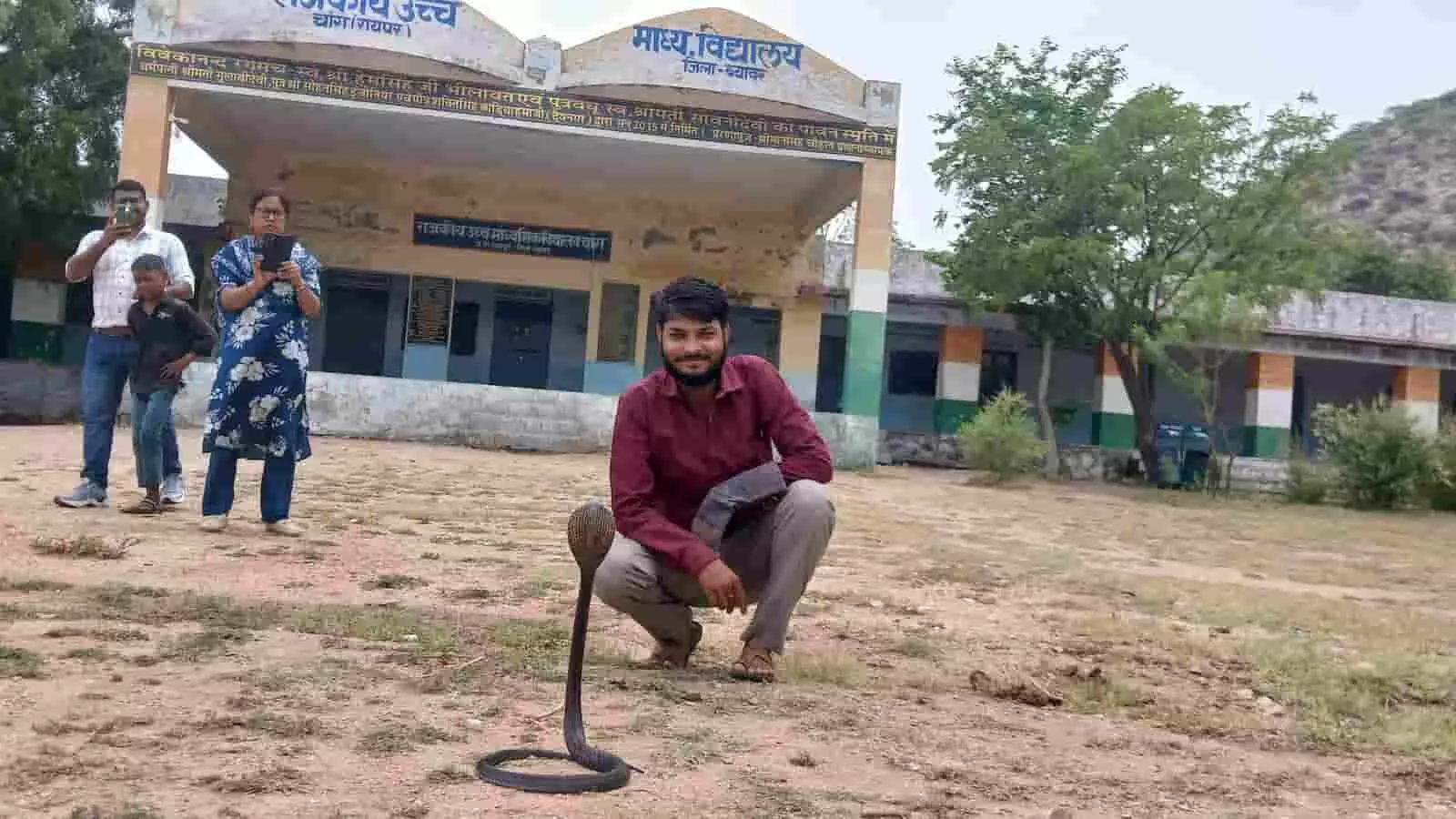 तस्वीर में ब्यावर के चांग स्कूल परिसर में जमीन पर फन फैलाए बैठा कोबरा सांप और उसके पास बैठा युवक दिख रहा है। तस्वीर में ब्यावर के चांग स्कूल परिसर में जमीन पर फन फैलाए बैठा कोबरा सांप और उसके पास बैठा युवक दिख रहा है।