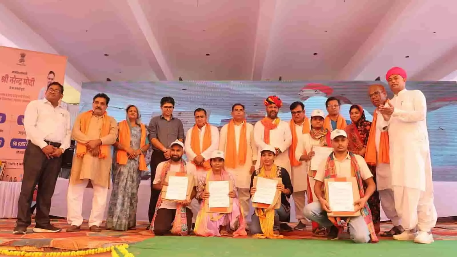 तस्वीर में दिख रही मंच पर उपस्थित अतिथियों की उपस्थिति में युवा नियुक्ति पत्र दिखा रहे हैं।