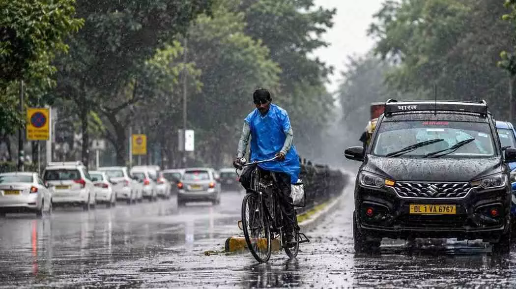 दिल्ली की सड़क पर बारिश में साइकिल चलाते व्यक्ति और कार, भारी बारिश का अलर्ट। दिल्ली की सड़क पर बारिश में साइकिल चलाते व्यक्ति और कार, भारी बारिश का अलर्ट।
