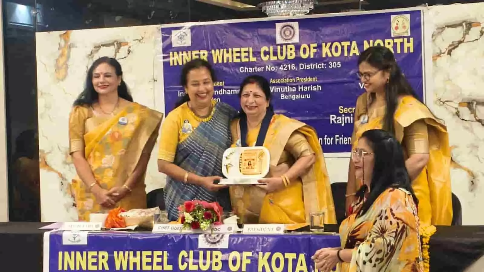 तस्वीर में कोटा के इनरव्हील क्लब समारोह में मंच पर महिला सदस्य स्मृति चिन्ह थामे हुए हैं।