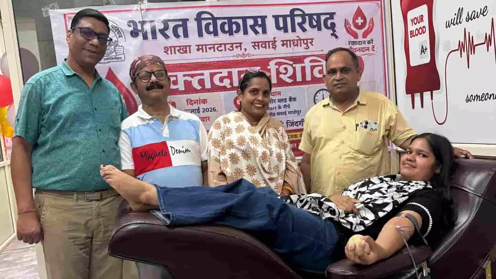 रक्तदान करते हुए एक युवती और पास में खड़े भारत विकास परिषद के सदस्य।