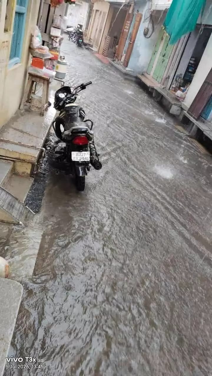 कानोड़ की बारिश से भरी गली में सड़क पर मोटरसाइकिल खड़ी दिखाई दे रही है।