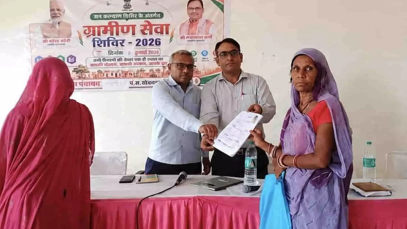 अधिकारी ग्रामीण सेवा शिविर में एक महिला को दस्तावेज प्रदान कर रहे हैं। अधिकारी ग्रामीण सेवा शिविर में एक महिला को दस्तावेज प्रदान कर रहे हैं।