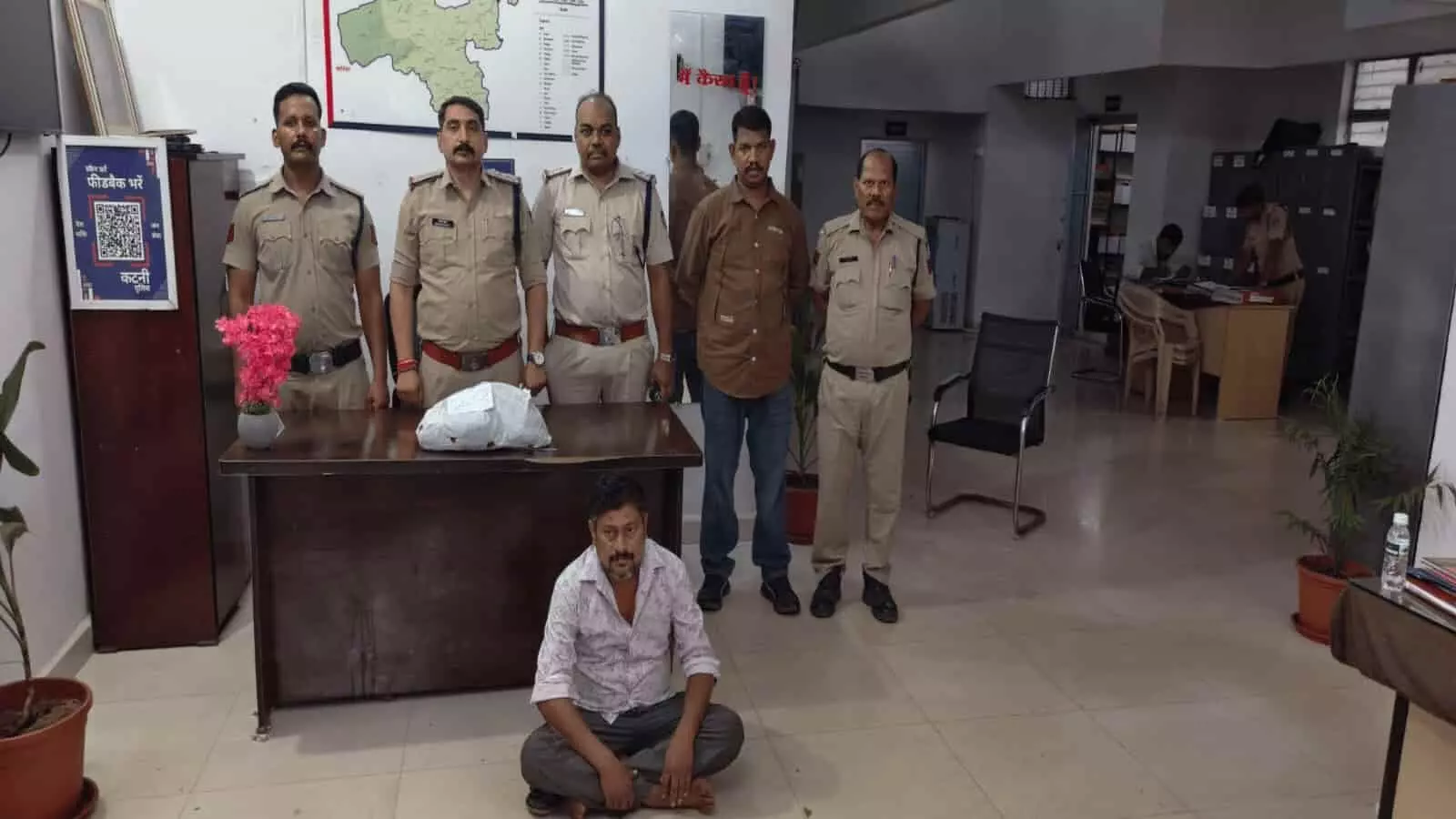 पुलिस टीम की हिरासत में बैठा आरोपी और मेज पर रखा गांजा।
