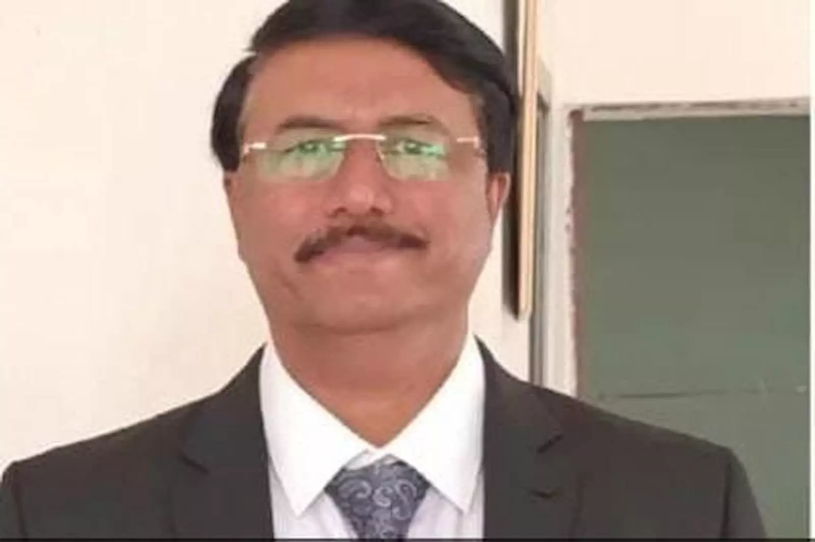 चश्मा और काले रंग का कोट-टाई पहने खड़े अधिकारी प्रमोद कुमार चतुर्वेदी की क्लोज-अप तस्वीर।