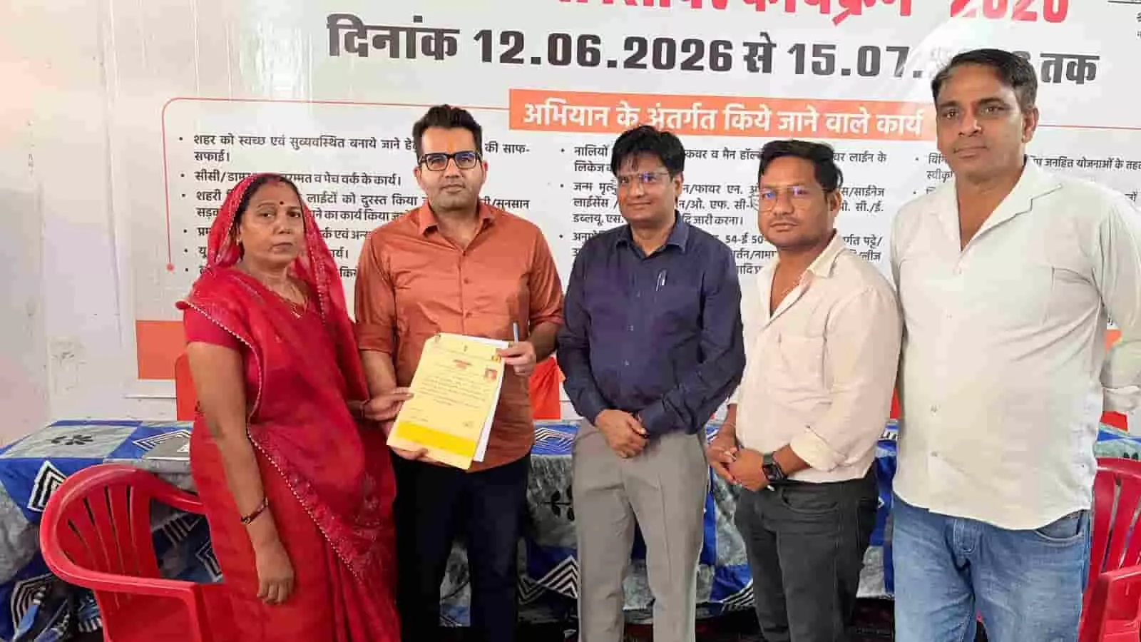 तस्वीर में मावली के शहरी सेवा शिविर के दौरान बैनर के सामने अधिकारी महिला को दस्तावेज देते हुए दिख रहे हैं।