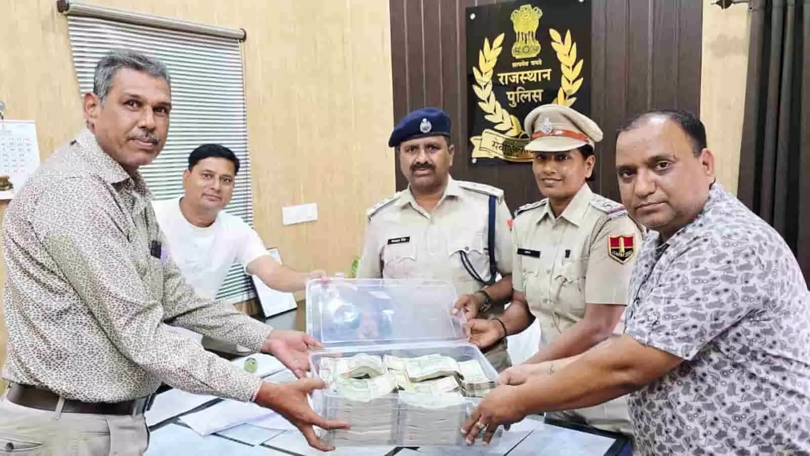 तस्वीर में पुलिस अधिकारी पीड़ित व्यक्ति को बरामद रुपयों से भरा बॉक्स सौंपते हुए दिख रहे हैं।