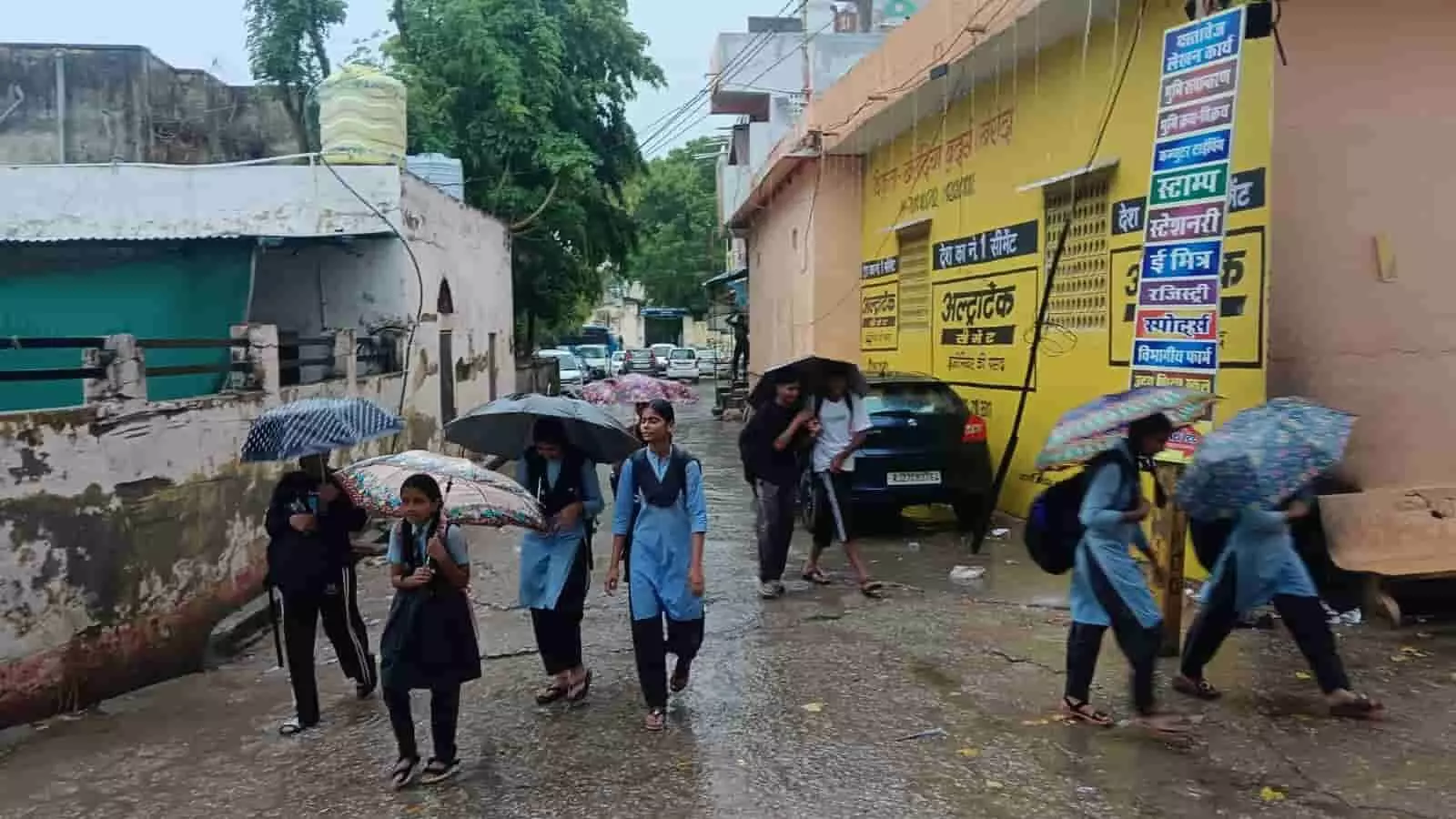 खेरोदा में बारिश के दौरान गीली सड़क पर छाता लेकर पैदल चलती स्कूली छात्राएं। खेरोदा में बारिश के दौरान गीली सड़क पर छाता लेकर पैदल चलती स्कूली छात्राएं।