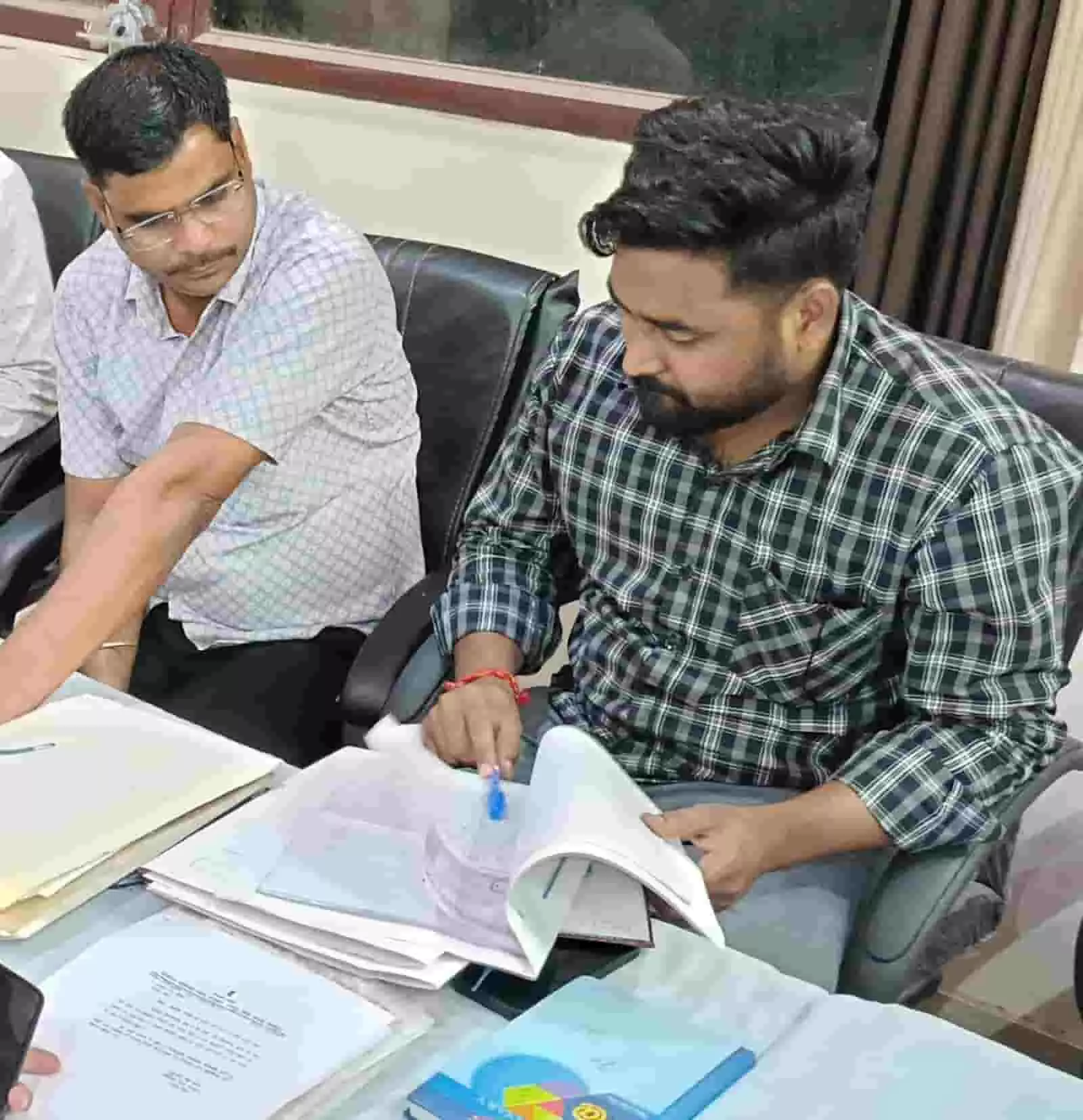 तस्वीर में मेज पर रखे सरकारी दस्तावेजों की समीक्षा करते हुए दो अधिकारी दिखाई दे रहे हैं। तस्वीर में मेज पर रखे सरकारी दस्तावेजों की समीक्षा करते हुए दो अधिकारी दिखाई दे रहे हैं।
