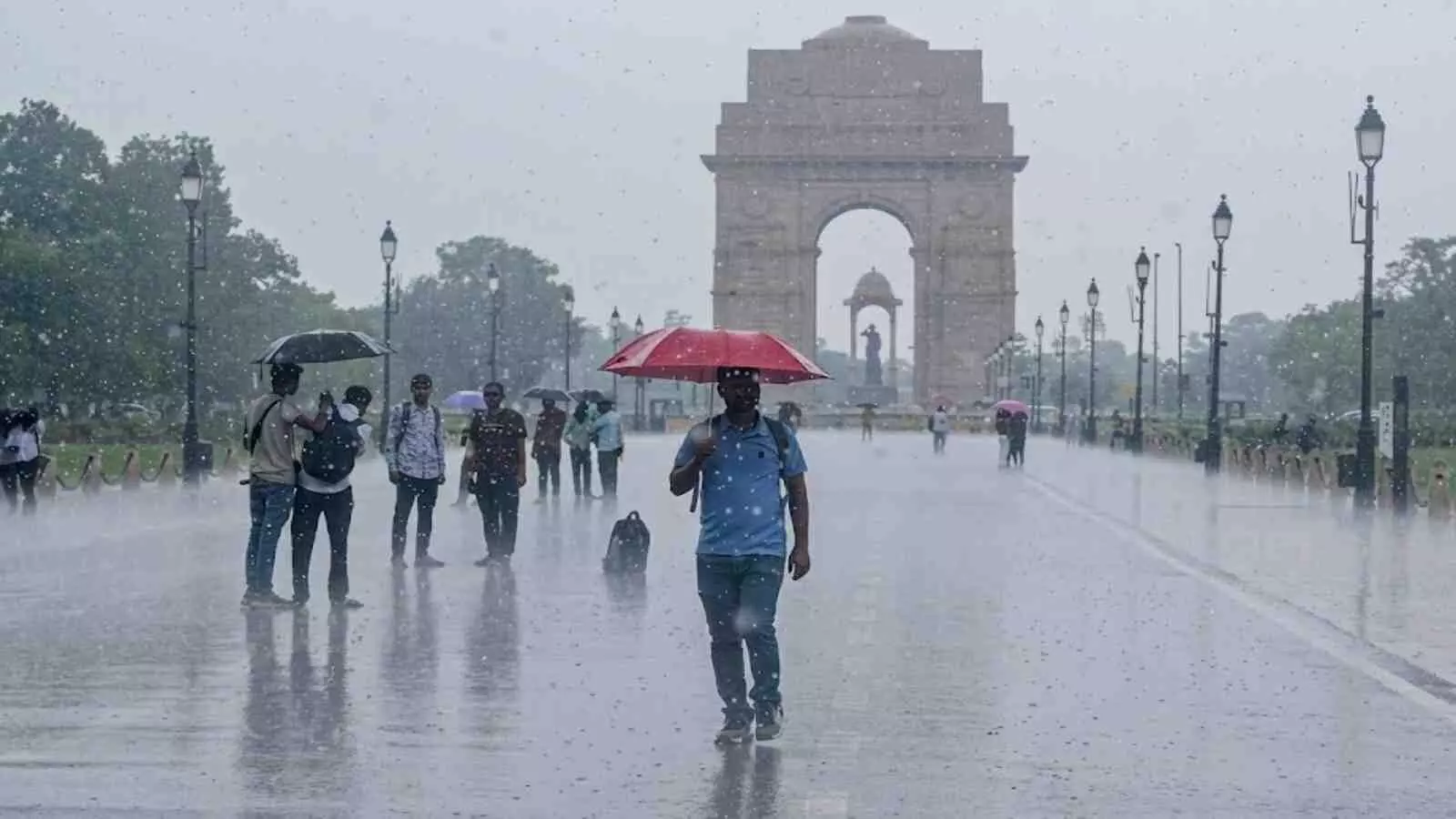 इंडिया गेट पर बारिश के दौरान छाता लेकर चलते लोग और खराब मौसम का दृश्य।