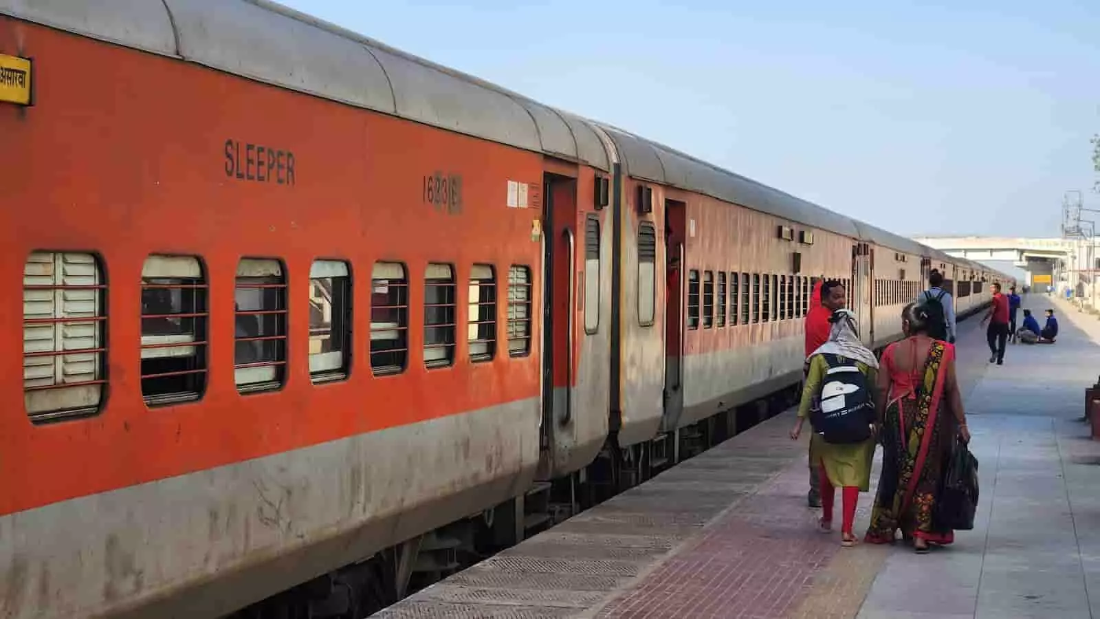 रेलवे स्टेशन के प्लेटफॉर्म पर खड़ी ट्रेन और उसके पास चलते हुए यात्री। रेलवे स्टेशन के प्लेटफॉर्म पर खड़ी ट्रेन और उसके पास चलते हुए यात्री।