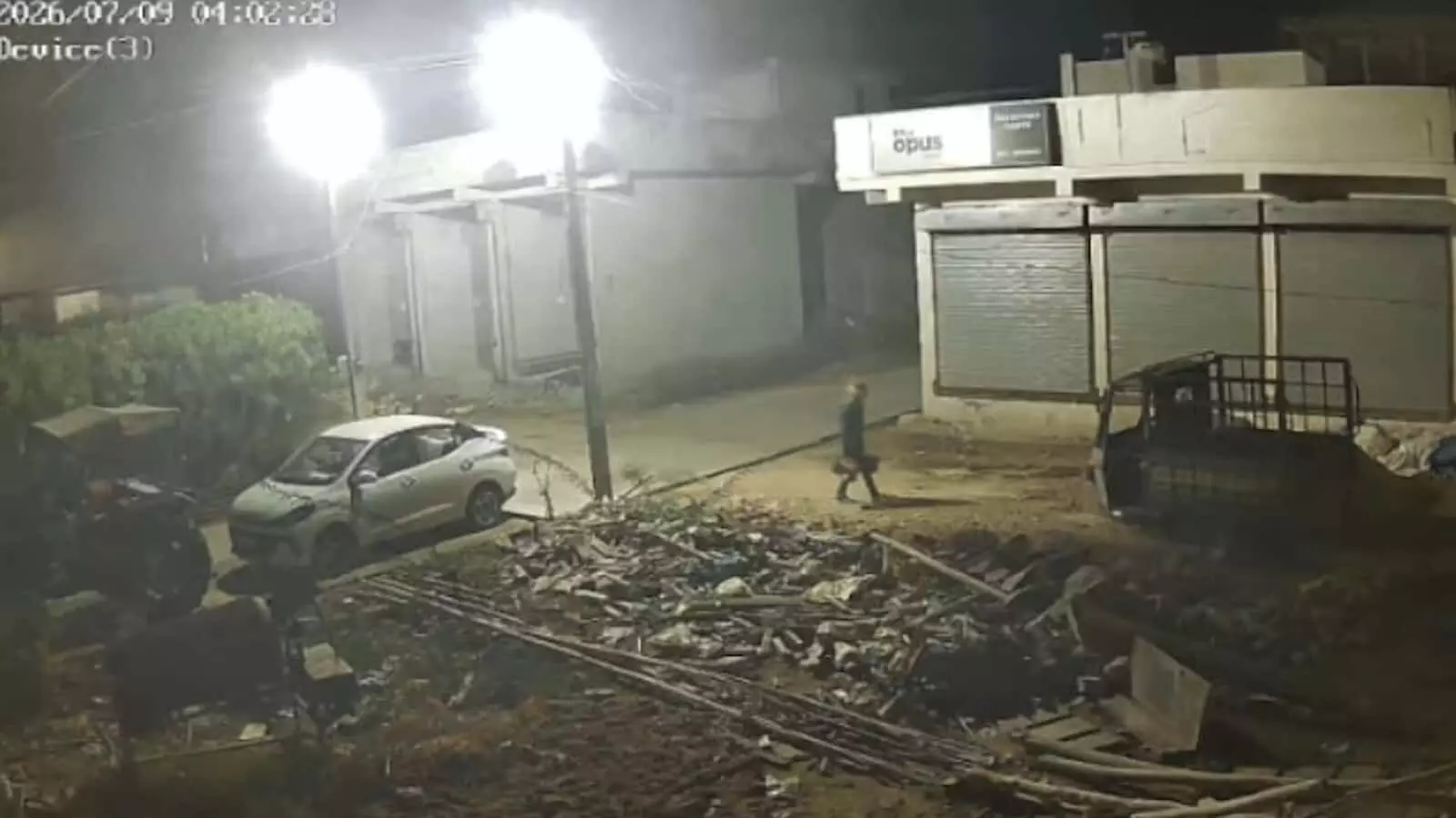 तस्वीर में रात के समय एक व्यक्ति बंद दुकानों के सामने सड़क पर चलता दिख रहा है। तस्वीर में रात के समय एक व्यक्ति बंद दुकानों के सामने सड़क पर चलता दिख रहा है।