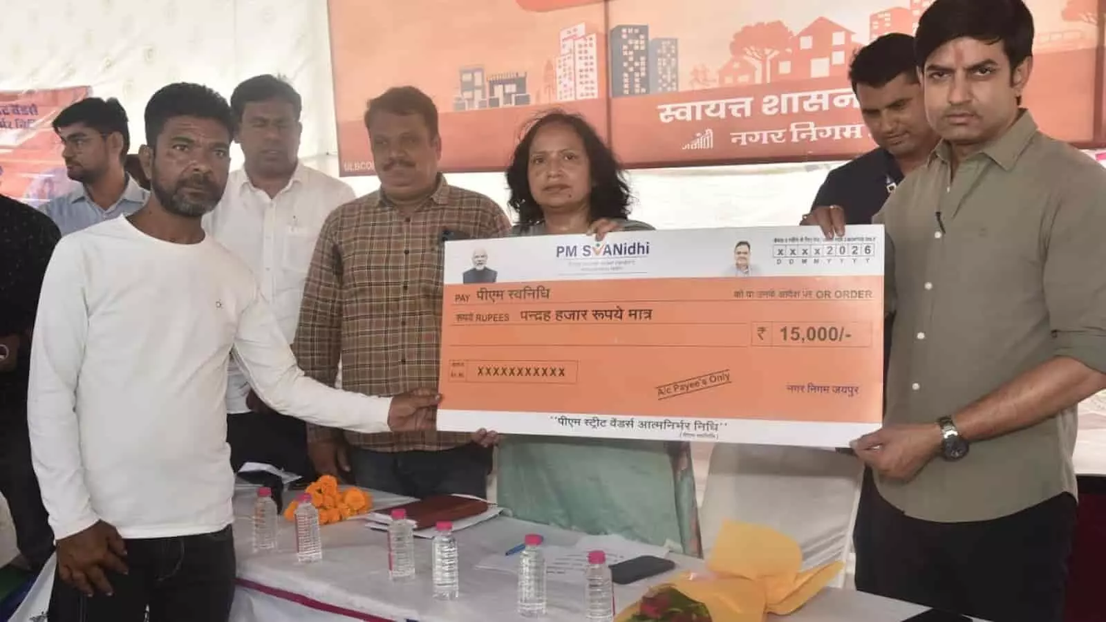 पीएम स्वनिधि योजना का डमी चेक पकड़े हुए विधायक और नागरिक जयपुर नगर निगम के सेवा शिविर में उपस्थित हैं।