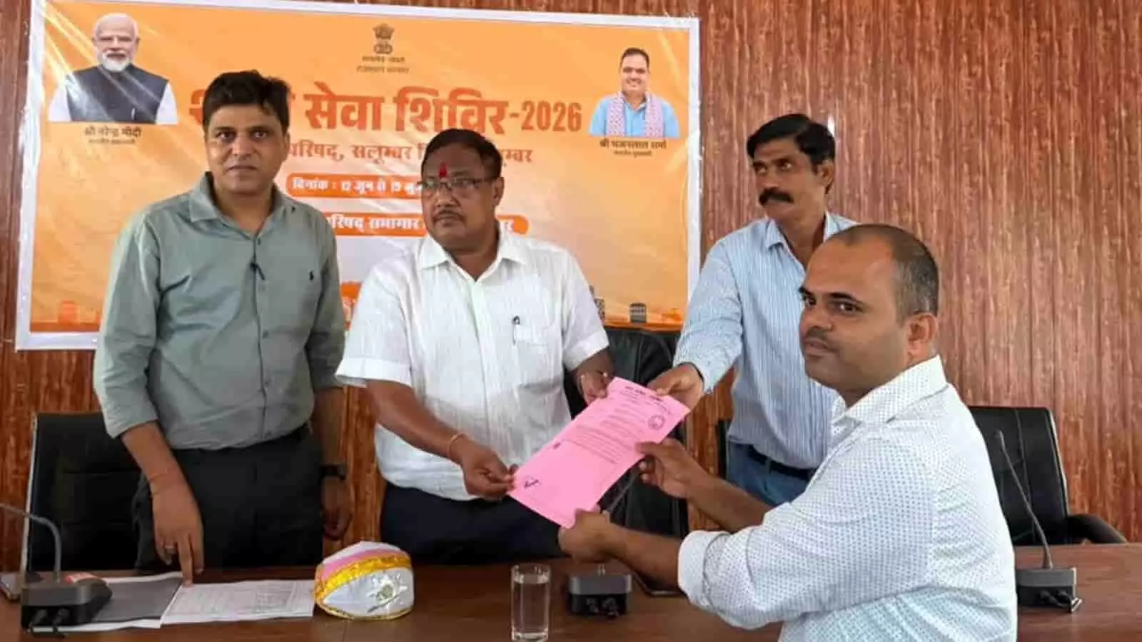 तस्वीर में शहरी सेवा शिविर के दौरान अधिकारी एक व्यक्ति को दस्तावेज वितरित करते हुए। तस्वीर में शहरी सेवा शिविर के दौरान अधिकारी एक व्यक्ति को दस्तावेज वितरित करते हुए।