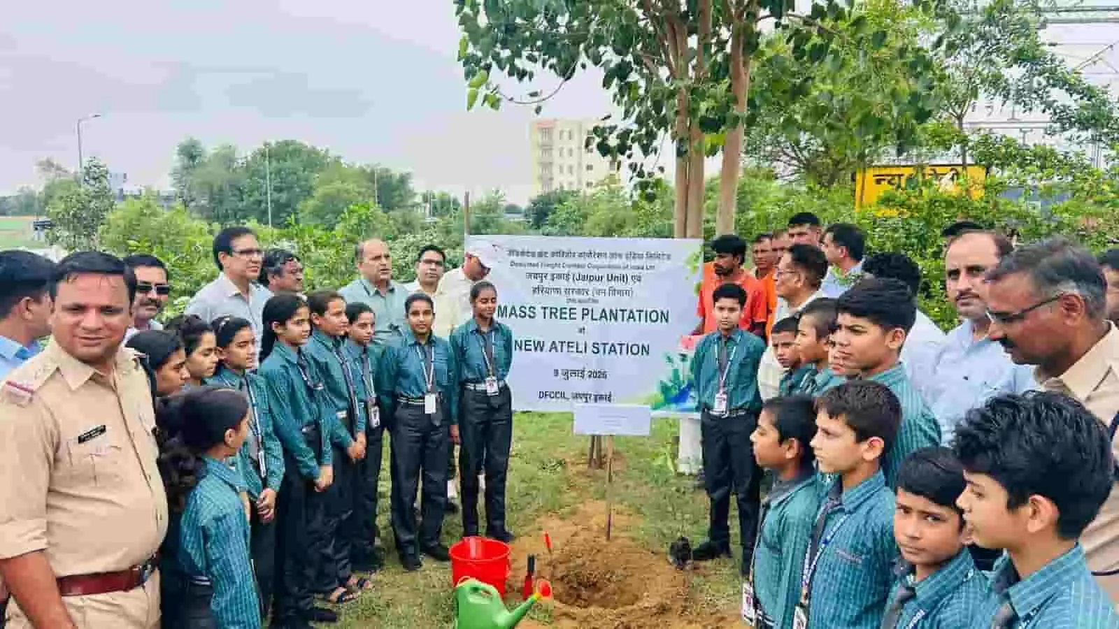 न्यू अटेली स्टेशन पर वृक्षारोपण अभियान के दौरान बैनर के पास खड़े अधिकारी और स्कूली बच्चे।