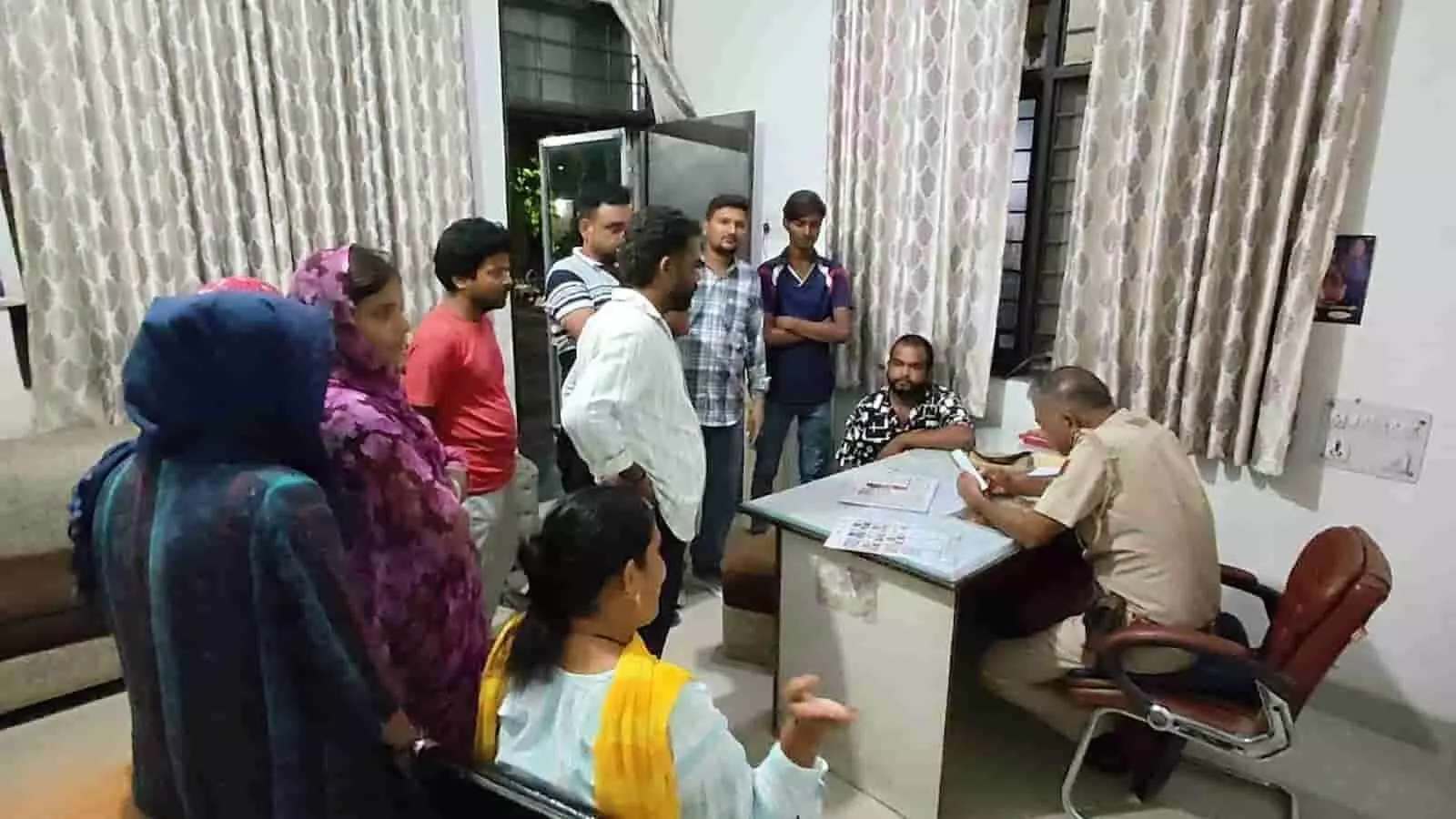 पुलिस थाने के कमरे में पुलिस अधिकारी के सामने शिकायत दर्ज कराने खड़े पीड़ित लोग। पुलिस थाने के कमरे में पुलिस अधिकारी के सामने शिकायत दर्ज कराने खड़े पीड़ित लोग।