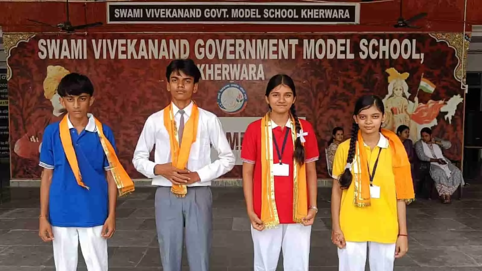 खेरवाड़ा स्कूल में बैनर के आगे गले में उपरना पहने खड़े चार विद्यार्थी। खेरवाड़ा स्कूल में बैनर के आगे गले में उपरना पहने खड़े चार विद्यार्थी।