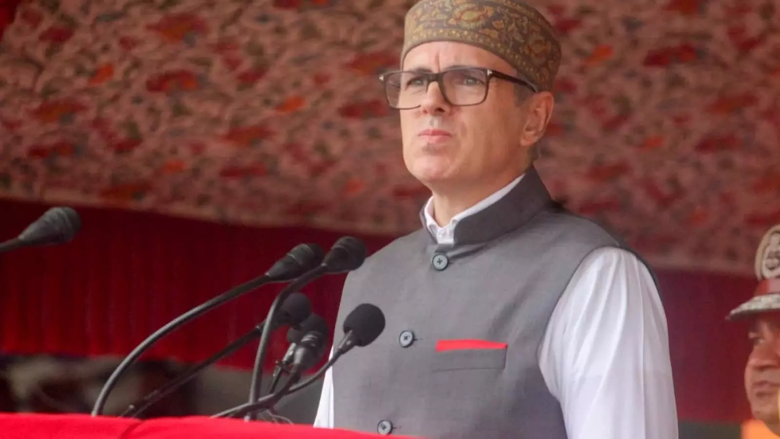 चश्मा पहने उमर अब्दुल्ला एक कार्यक्रम में मंच से संबोधित कर रहे हैं।