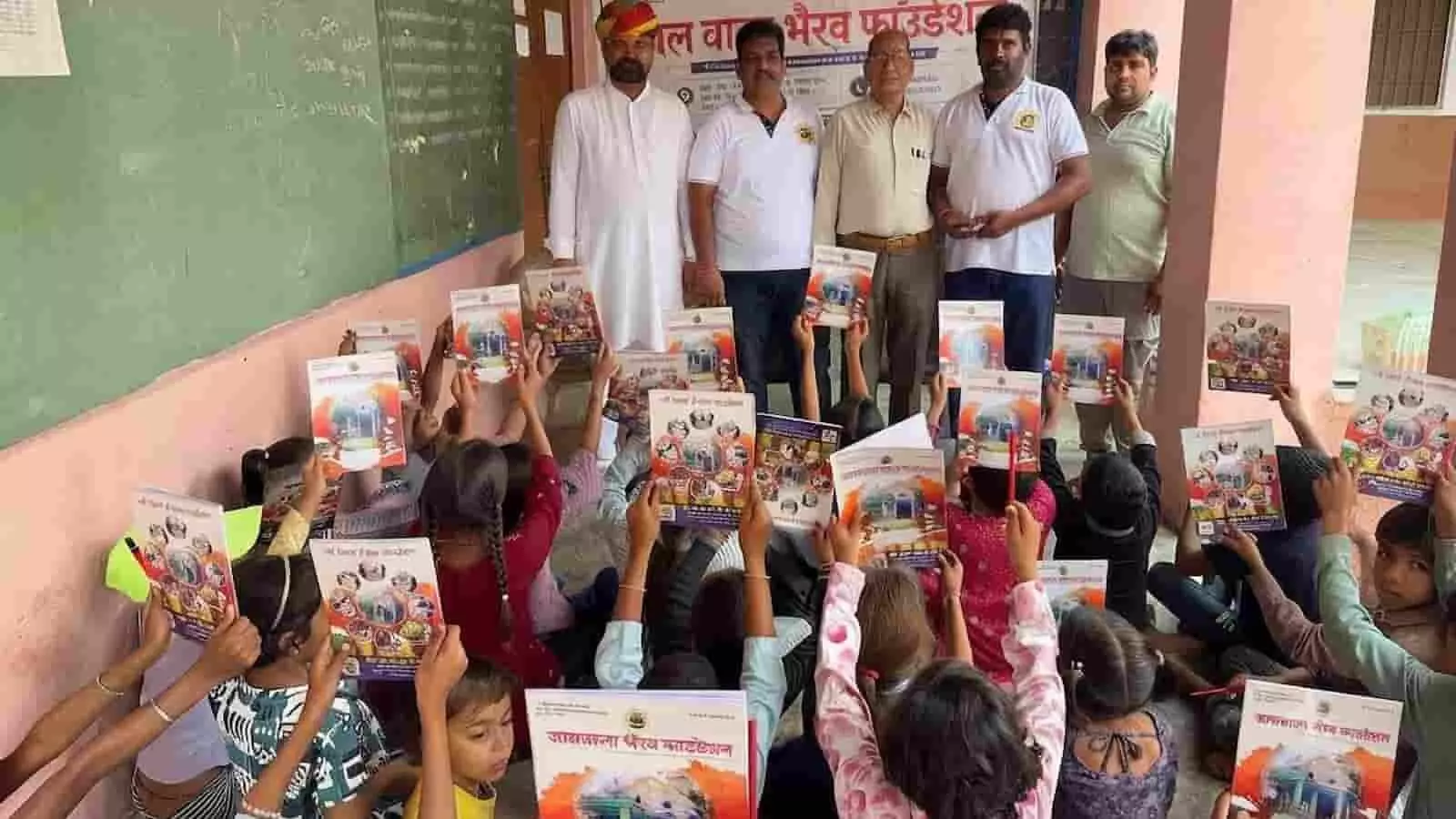 तस्वीर में एक सरकारी स्कूल के कमरे के भीतर बच्चे अपने हाथों में अभ्यास पुस्तिकाएं ऊपर उठाए हुए दिख रहे हैं।