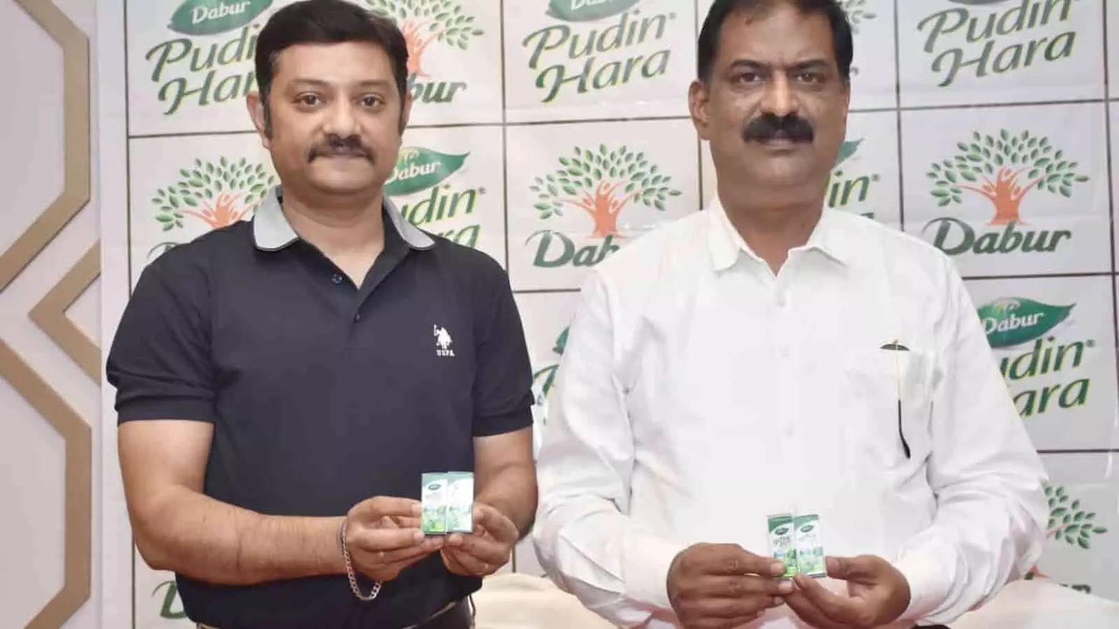 तस्वीर में डाबर बैकड्रॉप के सामने खड़े दो लोग पुदिन हरा उत्पाद दिखाते हुए। तस्वीर में डाबर बैकड्रॉप के सामने खड़े दो लोग पुदिन हरा उत्पाद दिखाते हुए।