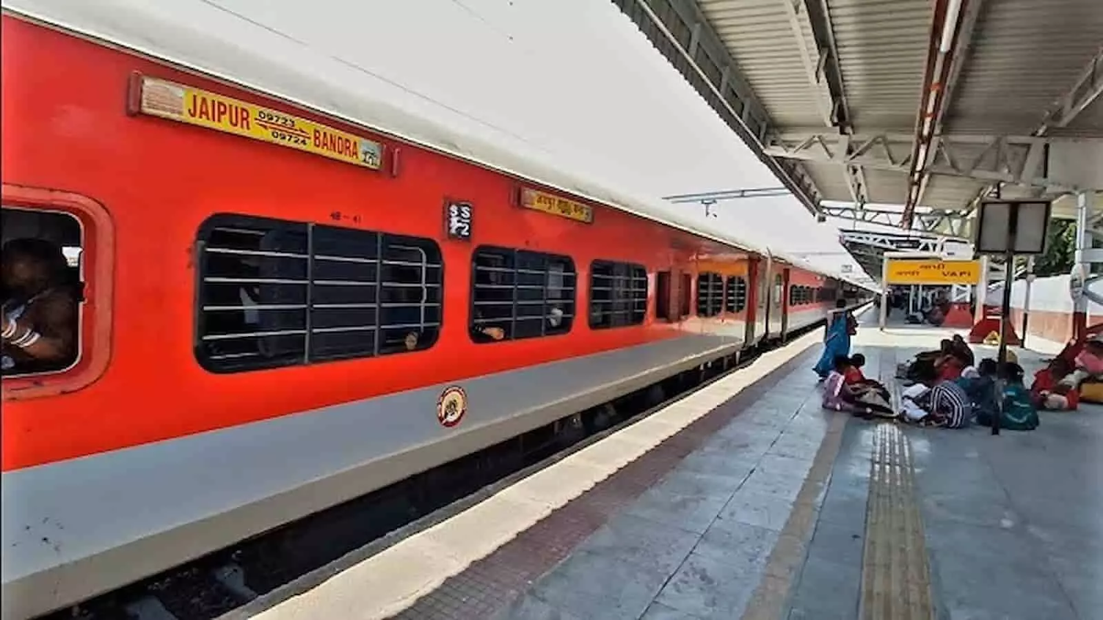 स्टेशन के प्लेटफॉर्म पर खड़ी यात्री ट्रेन और पास में बैठे यात्री।
