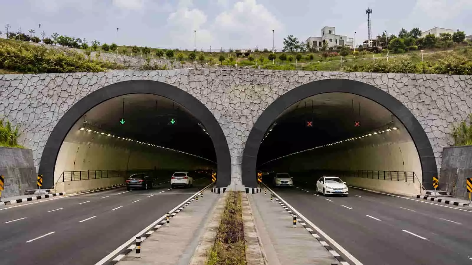 तस्वीर में एक आधुनिक सड़क टनल का प्रवेश द्वार और वाहन दिख रहे हैं। यह तस्वीर काल्पनिक है और एआई द्वारा केवल संदर्भ के लिए बनाई गई है।