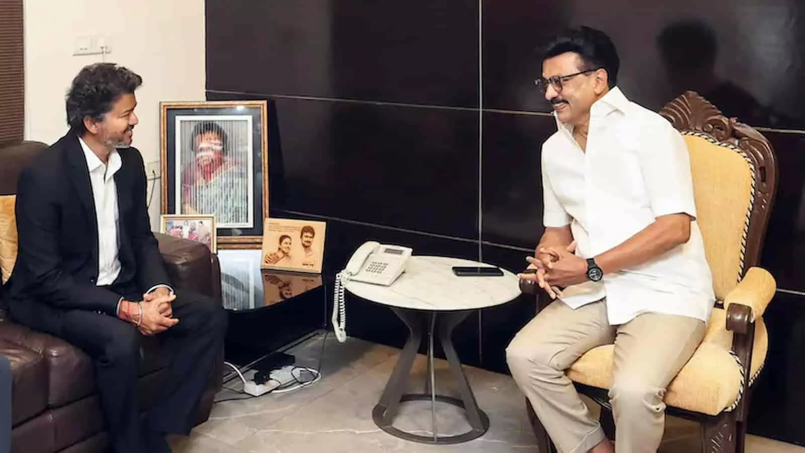 तस्वीर में विजय और एक व्यक्ति एक कमरे में सोफे पर बैठकर चर्चा कर रहे हैं।