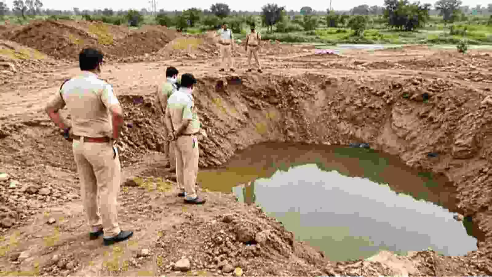 पुलिसकर्मी दिल्ली के जिंदपुर में खेतों के बीच बने पानी भरे गहरे गड्ढे देख रहे हैं।