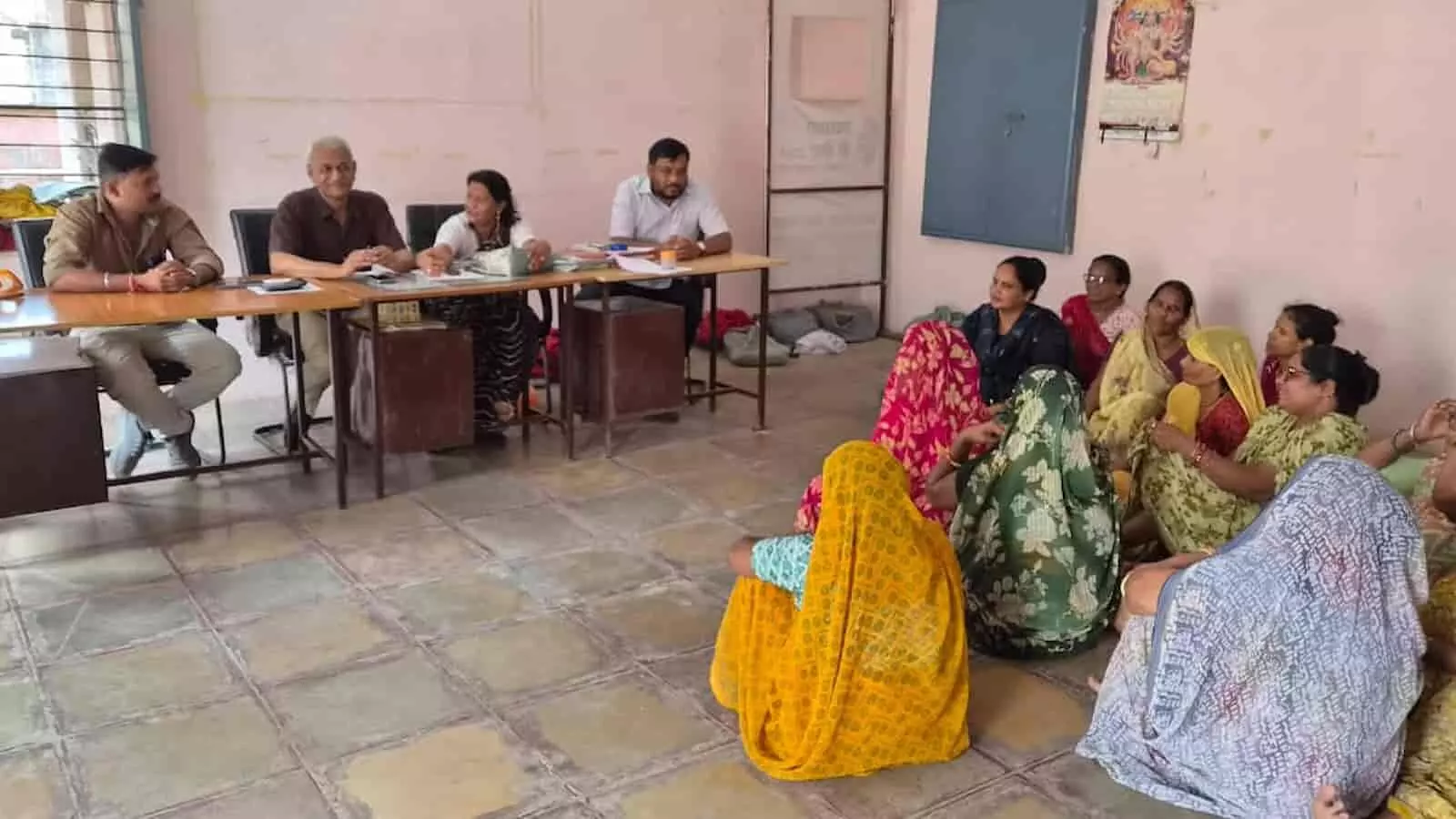 कार्यालय में मेज पर बैठे अधिकारी और फर्श पर बैठी सफाई महिला कर्मी। कार्यालय में मेज पर बैठे अधिकारी और फर्श पर बैठी सफाई महिला कर्मी।