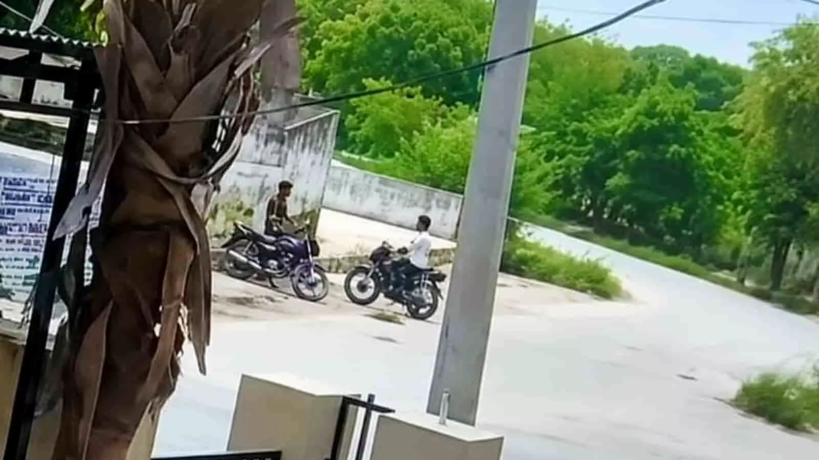 तस्वीर में सड़क किनारे दो युवक मोटरसाइकिल पर सवार नजर आ रहे हैं।
