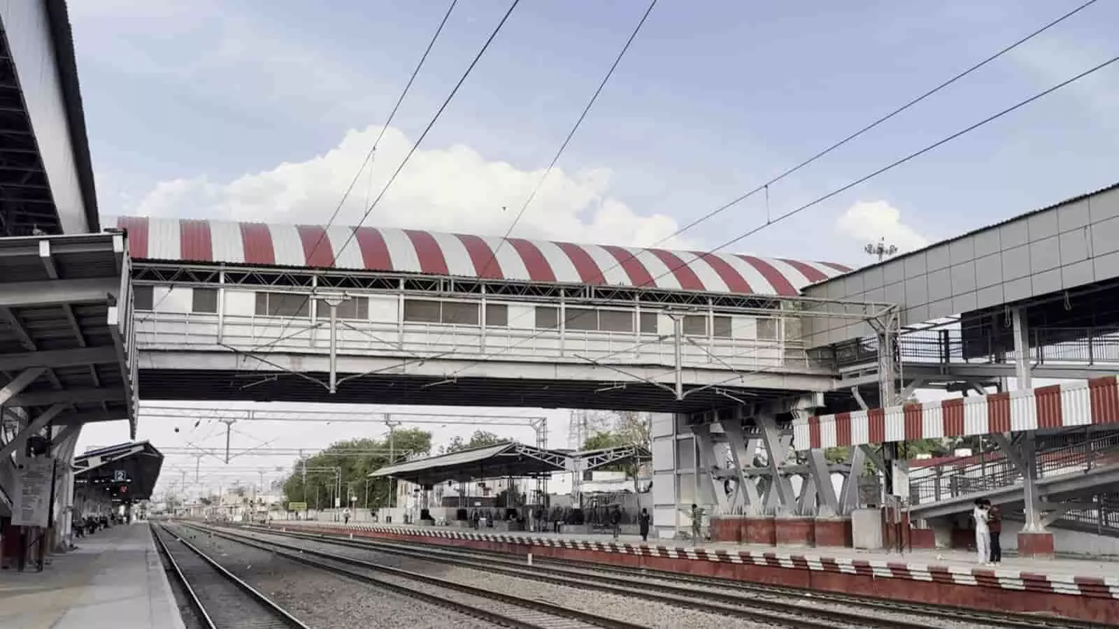 तस्वीर में दौसा रेलवे स्टेशन पर ऊपरी पैदल पुल, प्लेटफॉर्म, रेलवे ट्रैक और यात्री दिखाई दे रहे हैं।