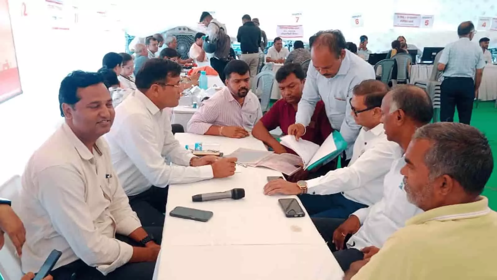 तस्वीर में अधिकारी और नागरिक मेज पर दस्तावेजों की जांच करते हुए शिविर स्थल पर दिखाई दे रहे हैं।