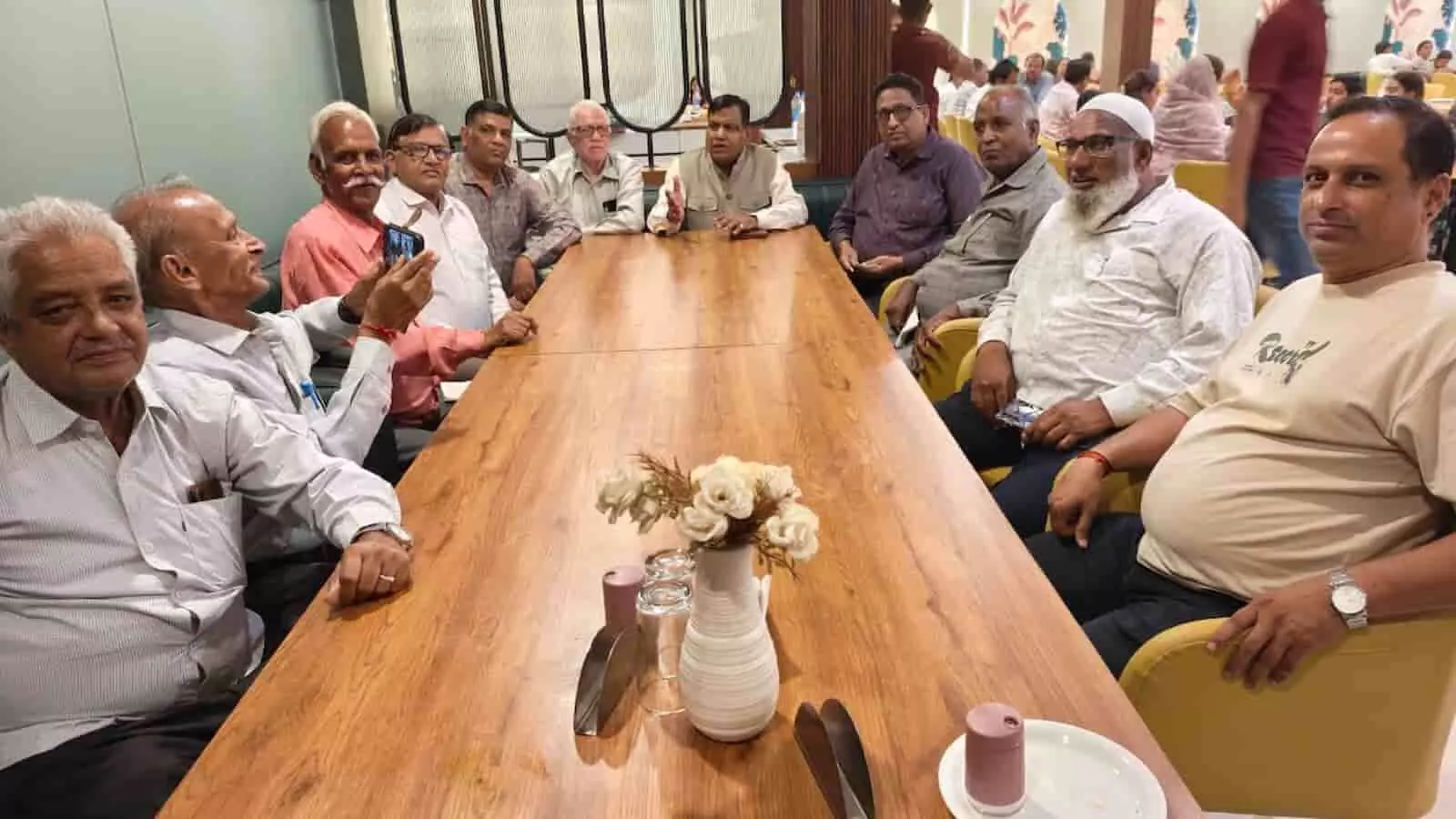तस्वीर में समिति सदस्य सभागार के भीतर बैठक के दौरान टेबल के चारों ओर बैठे हैं।