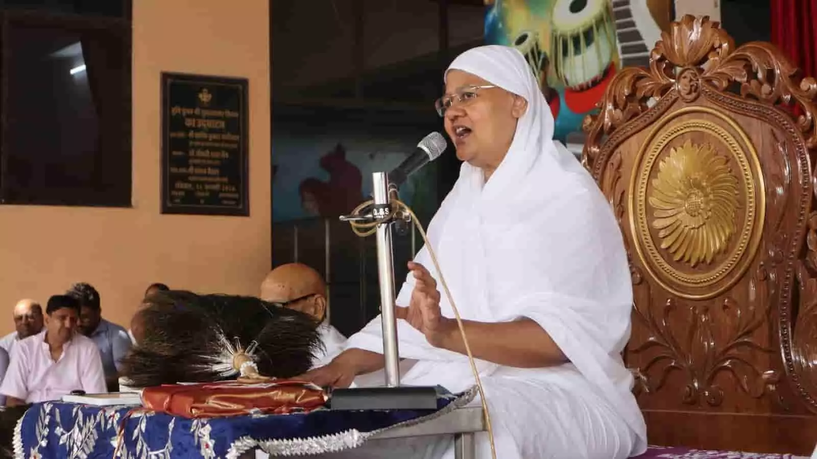 मंच पर बैठकर माइक के सामने धार्मिक प्रवचन देती हुईं सफेद वस्त्रों में आर्यिका श्री स्वस्तिभूषण माताजी। मंच पर बैठकर माइक के सामने धार्मिक प्रवचन देती हुईं सफेद वस्त्रों में आर्यिका श्री स्वस्तिभूषण माताजी।