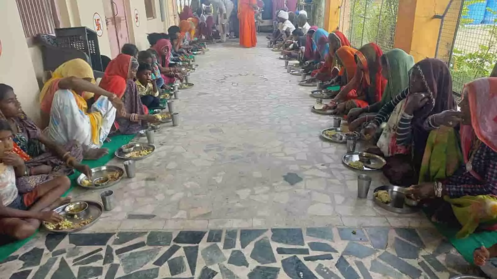 आश्रम परिसर में जमीन पर बैठकर पत्तल-थाली में भंडारे का प्रसाद खाते हुए पुरुष और महिलाएं। आश्रम परिसर में जमीन पर बैठकर पत्तल-थाली में भंडारे का प्रसाद खाते हुए पुरुष और महिलाएं।