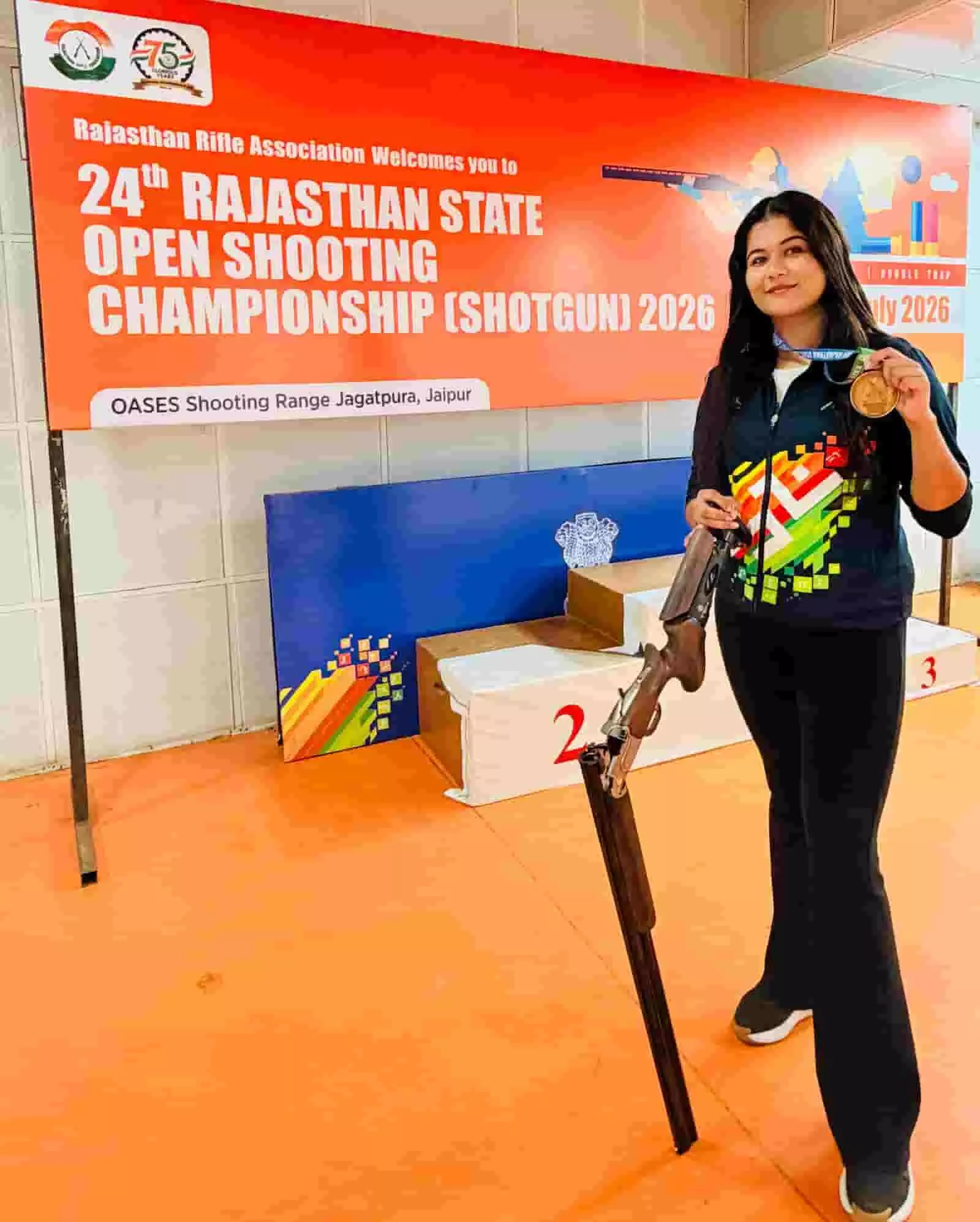 हाथ में बंदूक और गोल्ड मेडल पकड़े शूटर नांदिका सिंह जयपुर में मंच पर खड़ी हैं। हाथ में बंदूक और गोल्ड मेडल पकड़े शूटर नांदिका सिंह जयपुर में मंच पर खड़ी हैं।