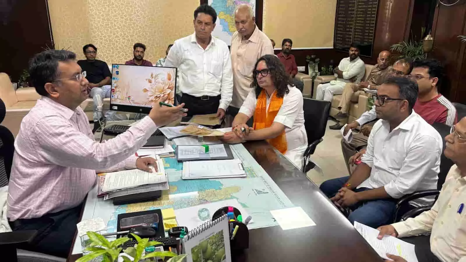 तस्वीर में कार्यालय की मेज पर सरकारी अधिकारियों और विधायक बालमुकुंदाचार्य के बीच बैठक का दृश्य। तस्वीर में कार्यालय की मेज पर सरकारी अधिकारियों और विधायक बालमुकुंदाचार्य के बीच बैठक का दृश्य।